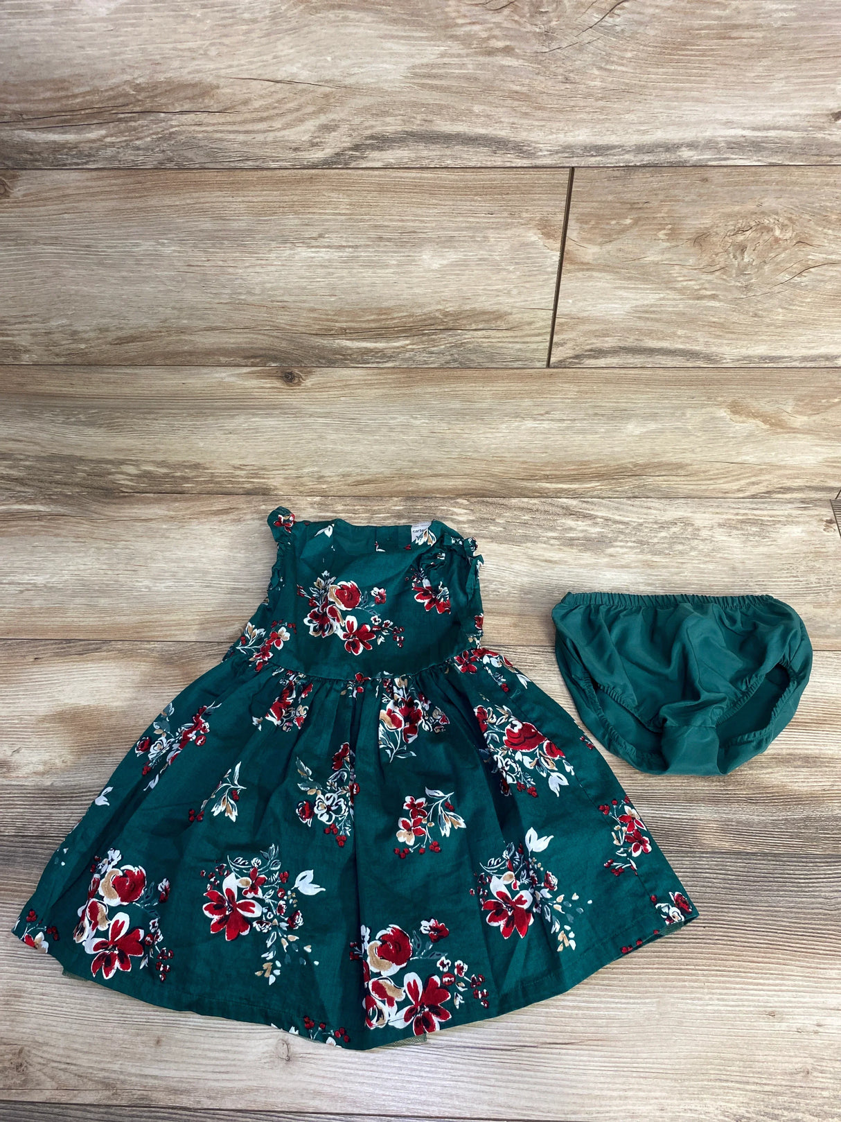 Green floral baby dress with matching diaper cover on wooden floor background