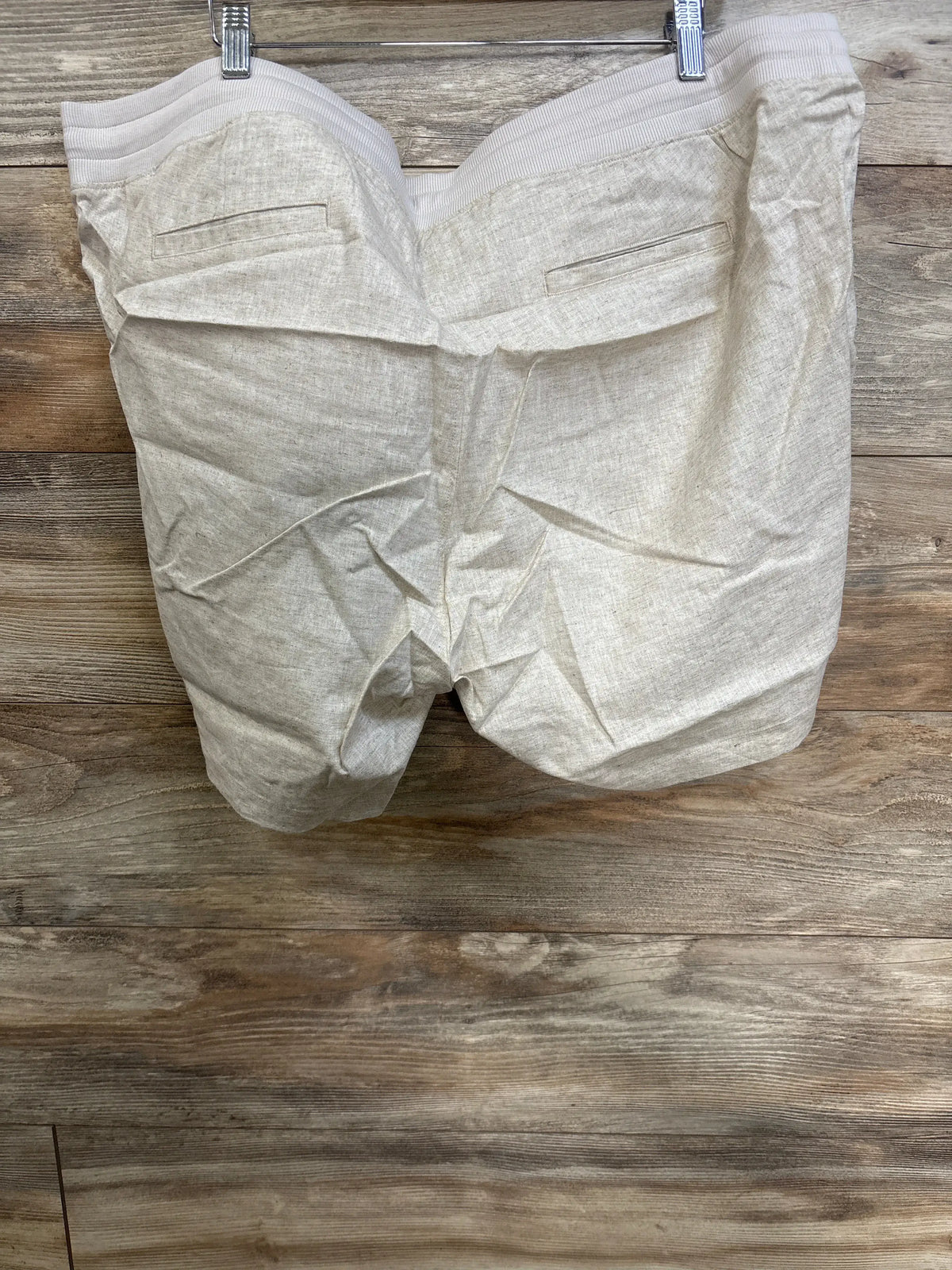 Back view of beige Gap maternity linen-blend shorts showcasing back welt pockets and elasticized waist on a wood backdrop