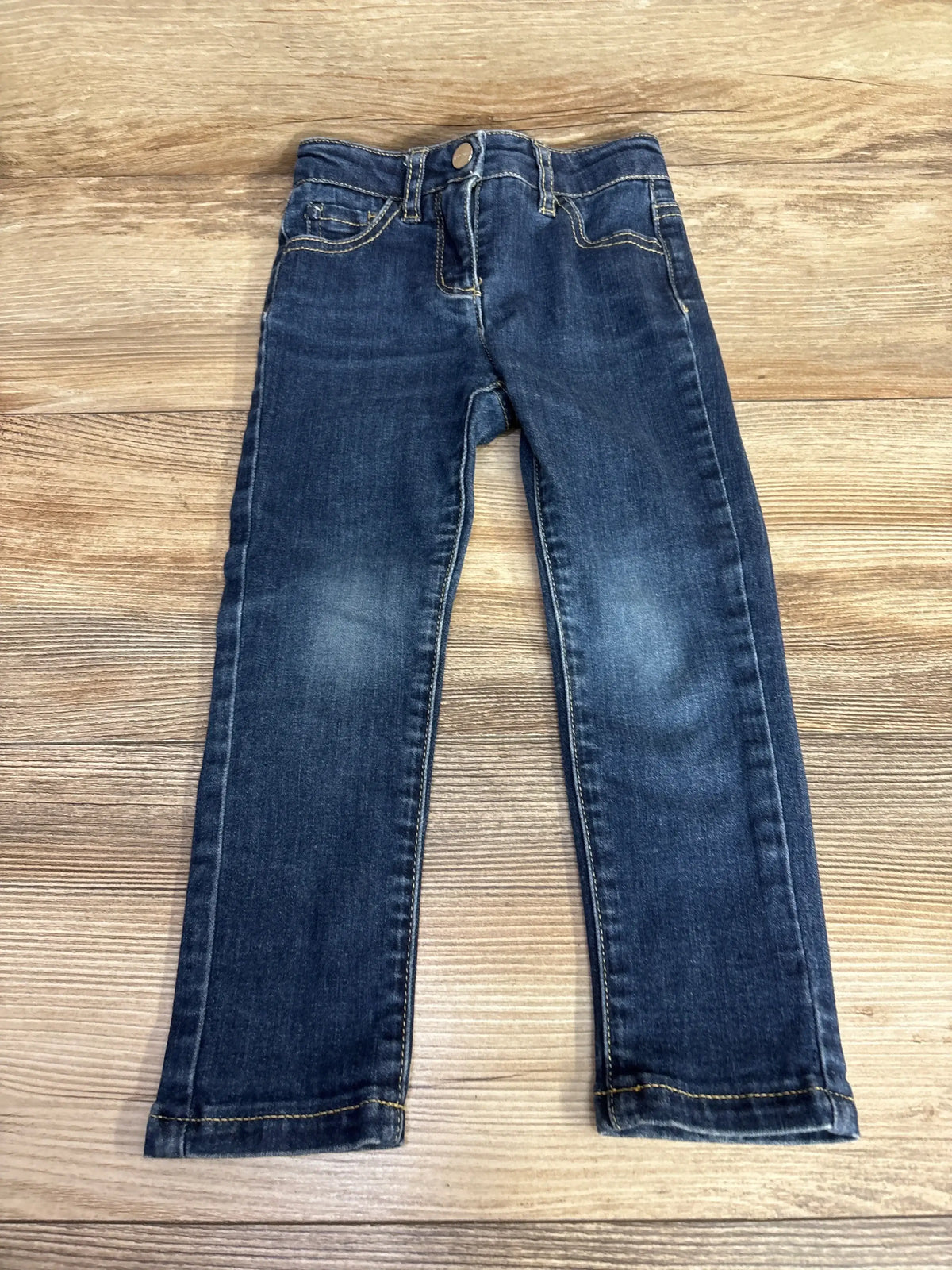 Dark wash kids' jeans with yellow stitching on wooden background