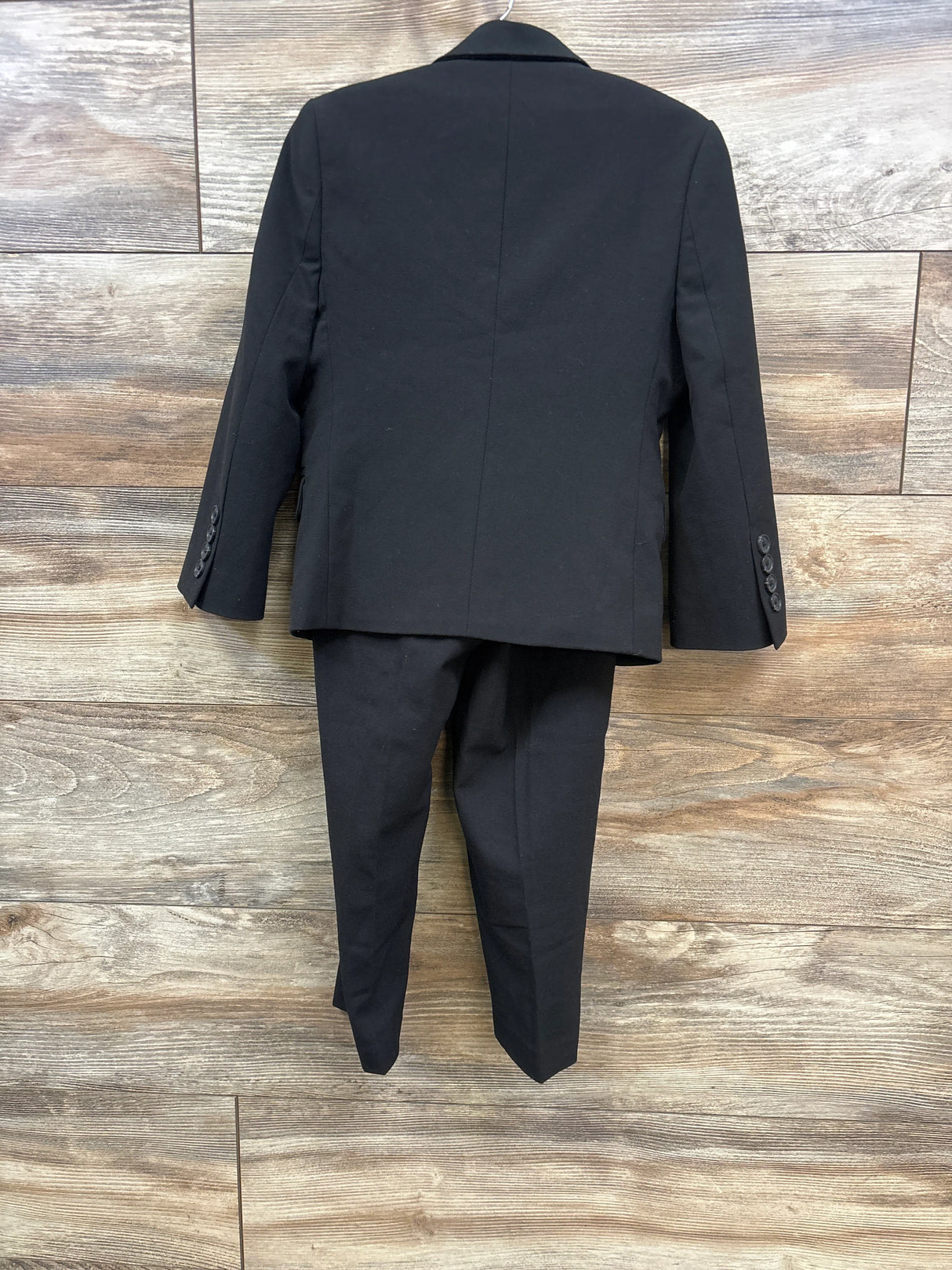 Back view of black formal suit jacket and pants hanging on wooden wall