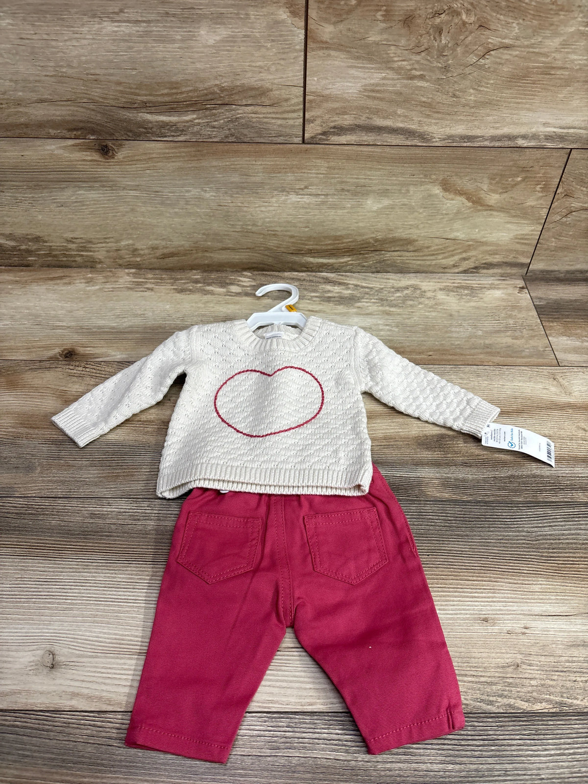 Flat lay of Carters 2pc knit sweater and pants set showcasing an ivory heart sweater and burgundy pants on wood flooring