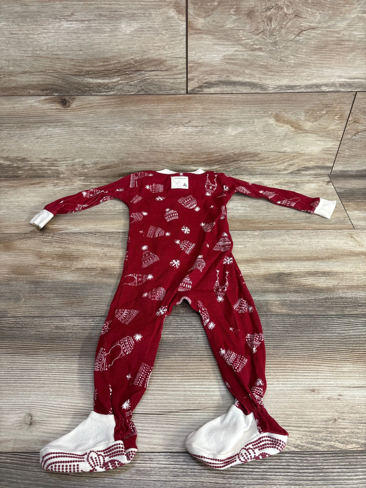 Red holiday-themed baby footed pajamas with white snowflake and reindeer print, laid flat on wood floor