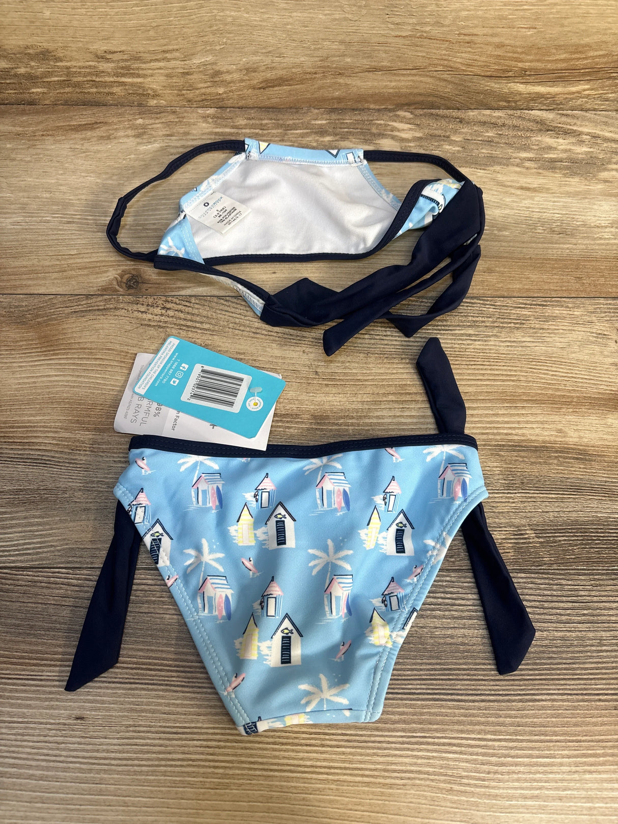 Blue girls' bikini with beach hut and palm tree print, side ties, on wooden background