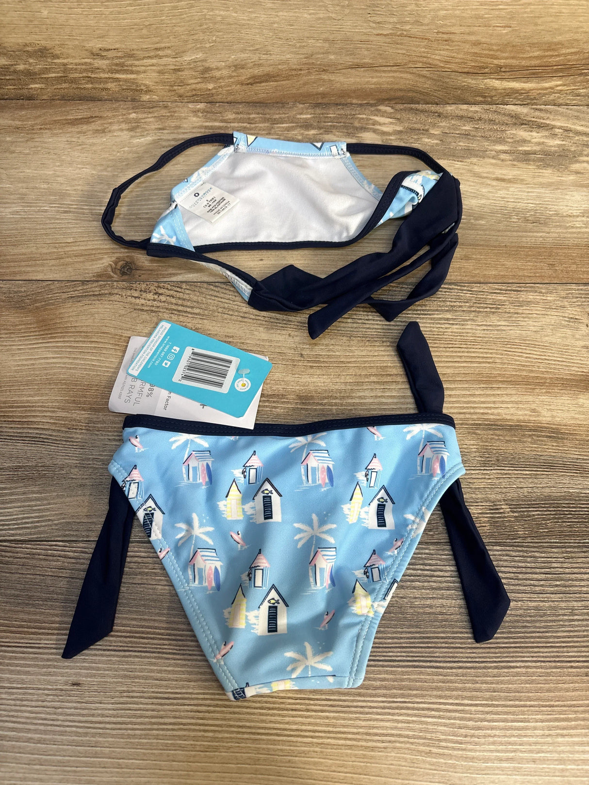 Blue girls' bikini with beach hut and palm tree print, side ties, on wooden background
