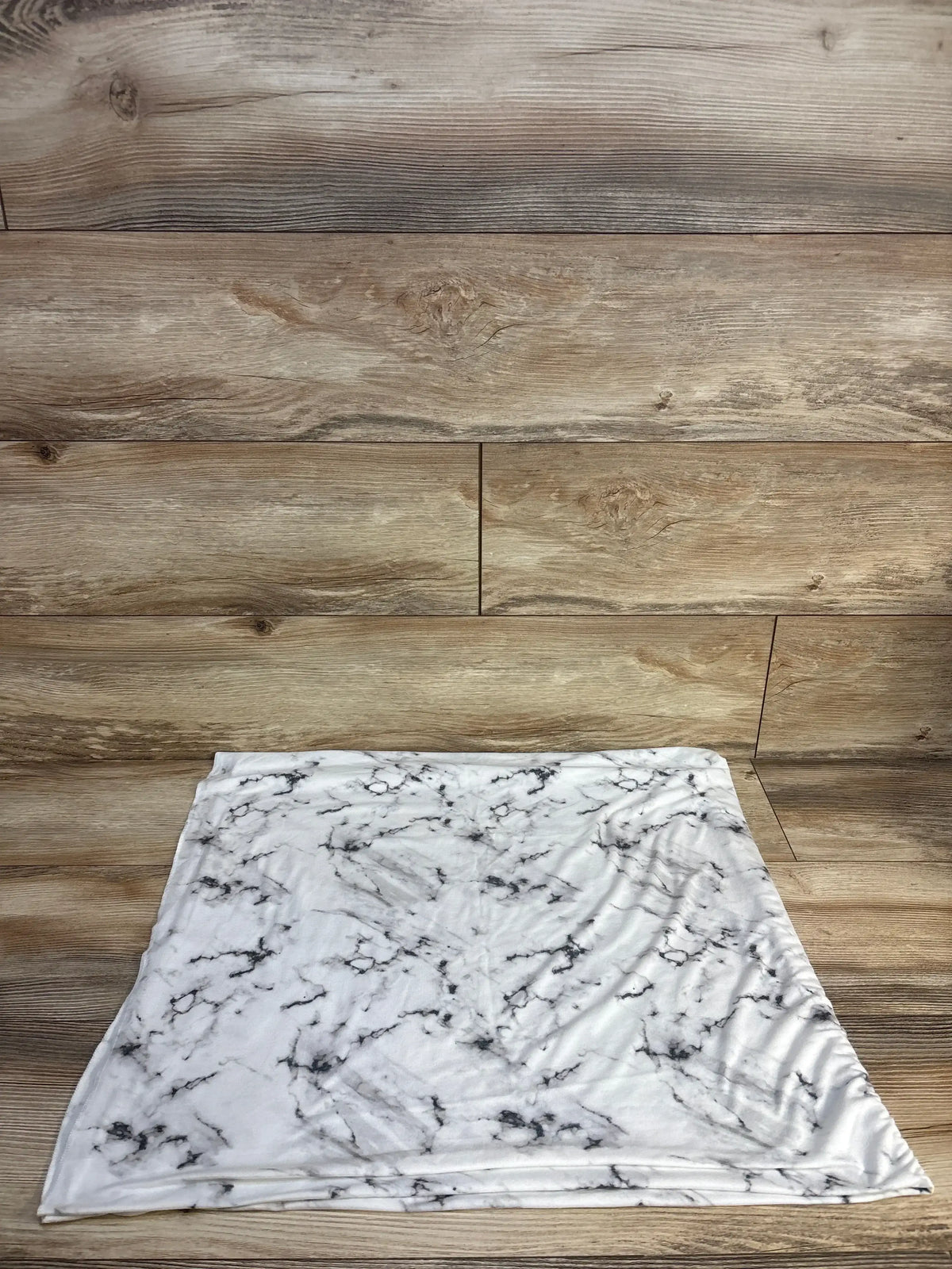 Flat-lay of Copper Pearl Knit Swaddle Blanket Marble White showcasing marble print and soft knit texture on a wooden floor