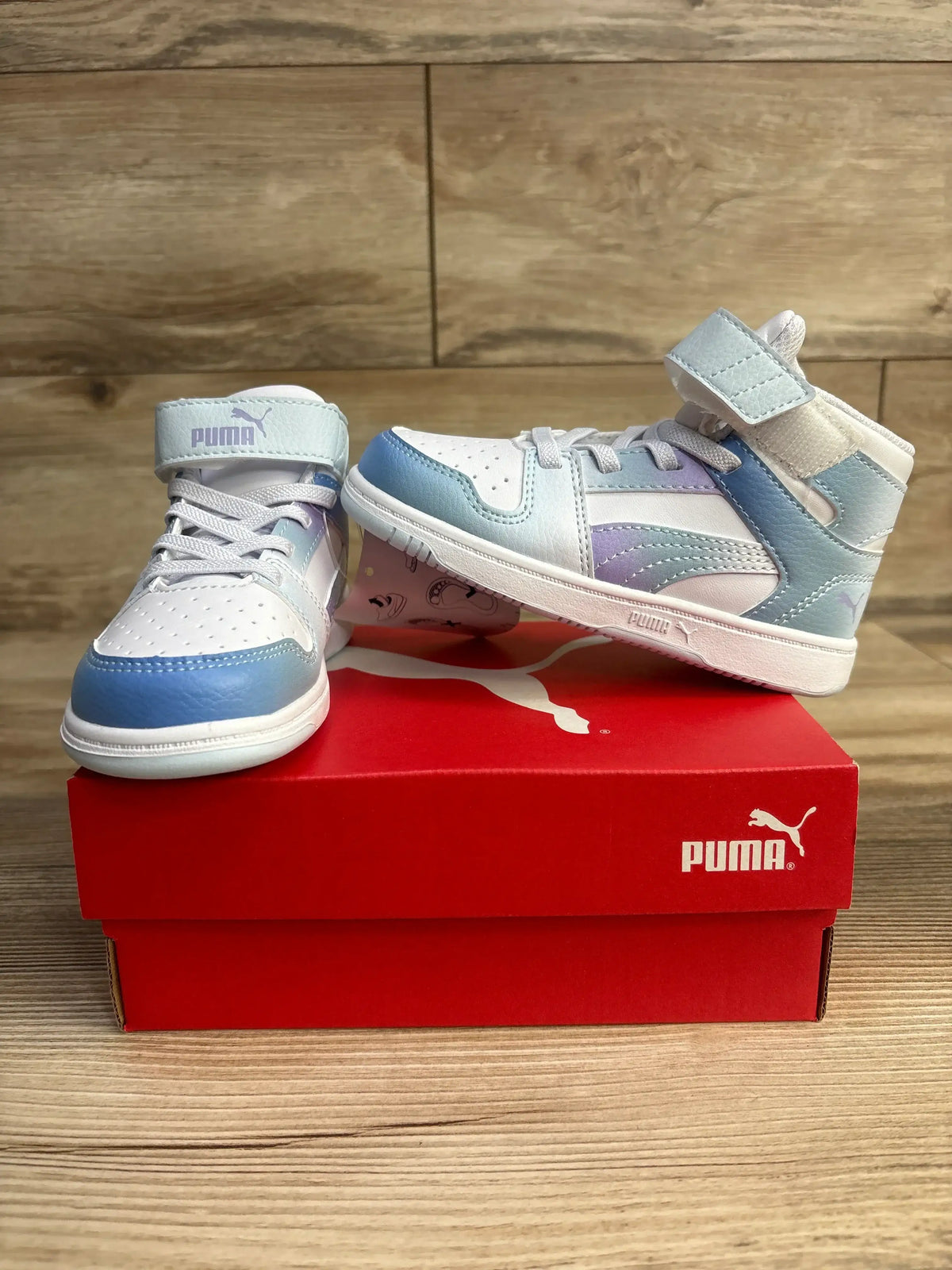 Pair of white and pastel blue Puma high-top sneakers on red Puma shoe box on wooden surface