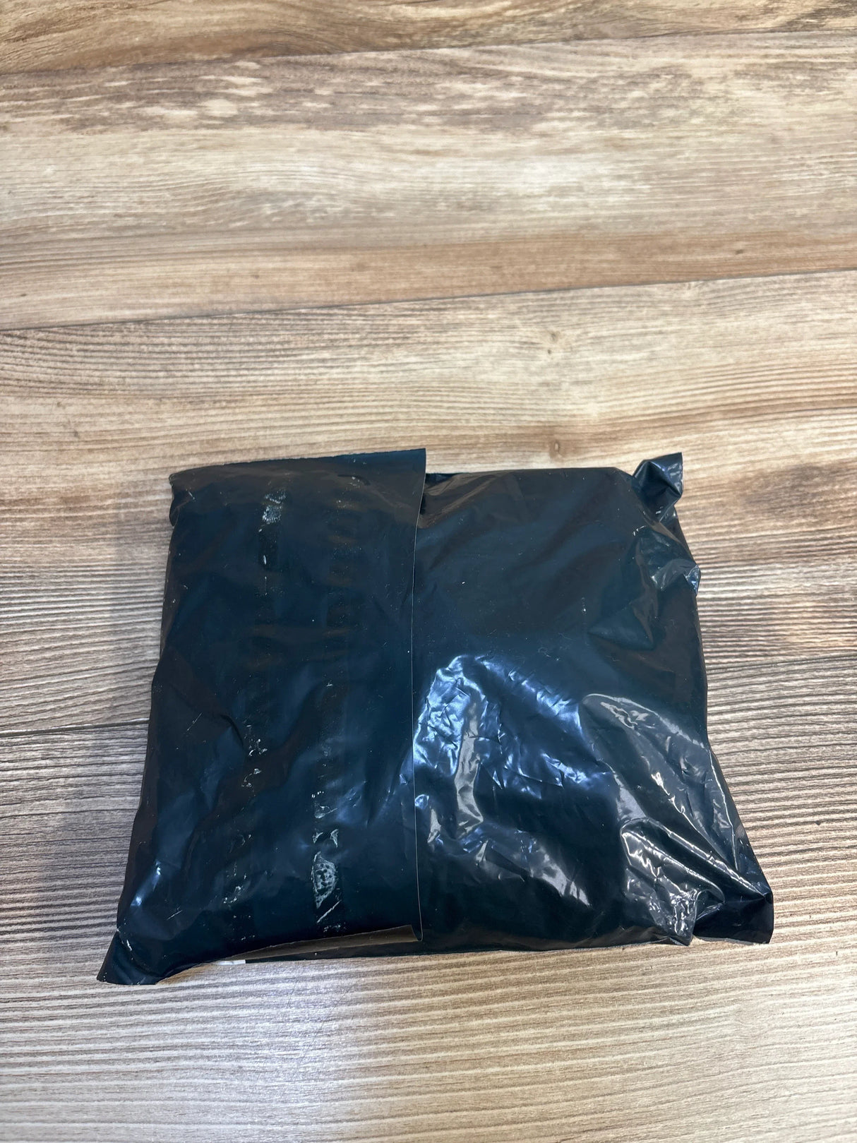 Sealed black plastic package on wood surface, kids resale shipping parcel