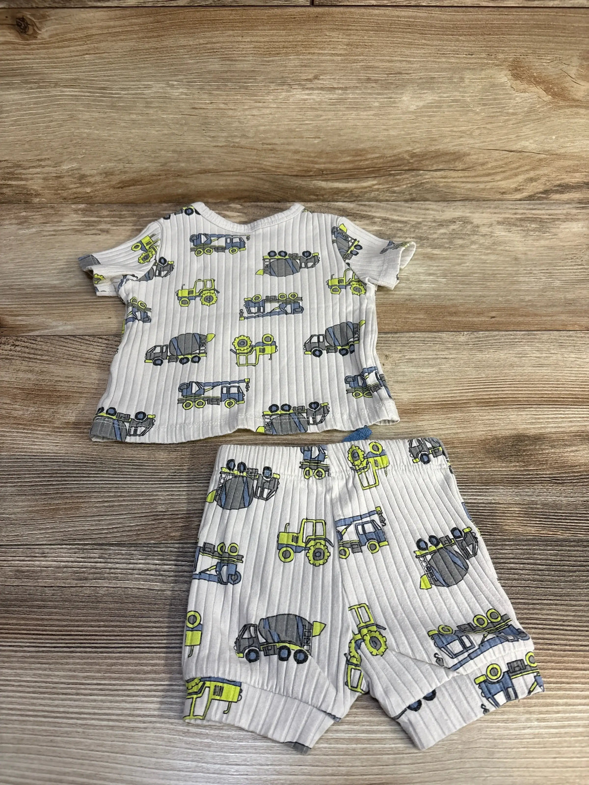 Flat lay of beige ribbed baby shirt and shorts with construction vehicle print and elastic waist on wood