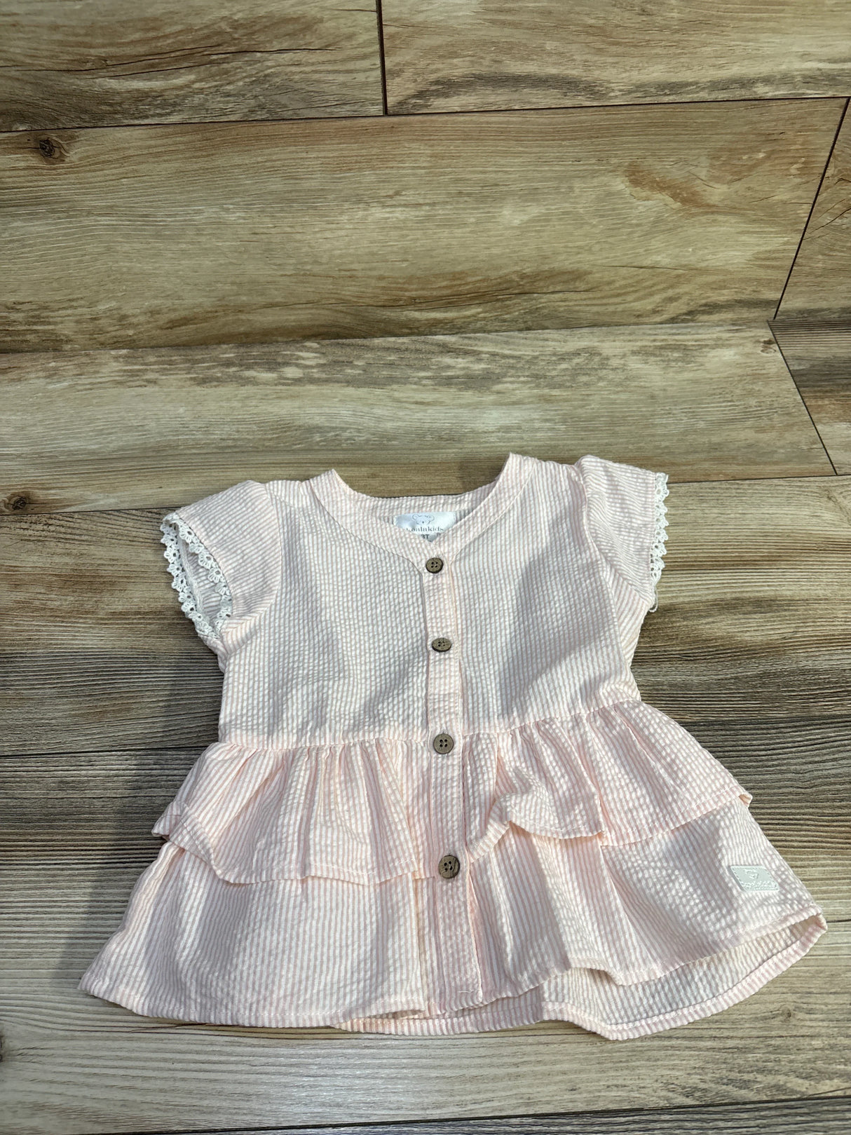 Flat lay of pink and white striped seersucker peplum top showing button-front and lace-trim cap sleeves on wood floor