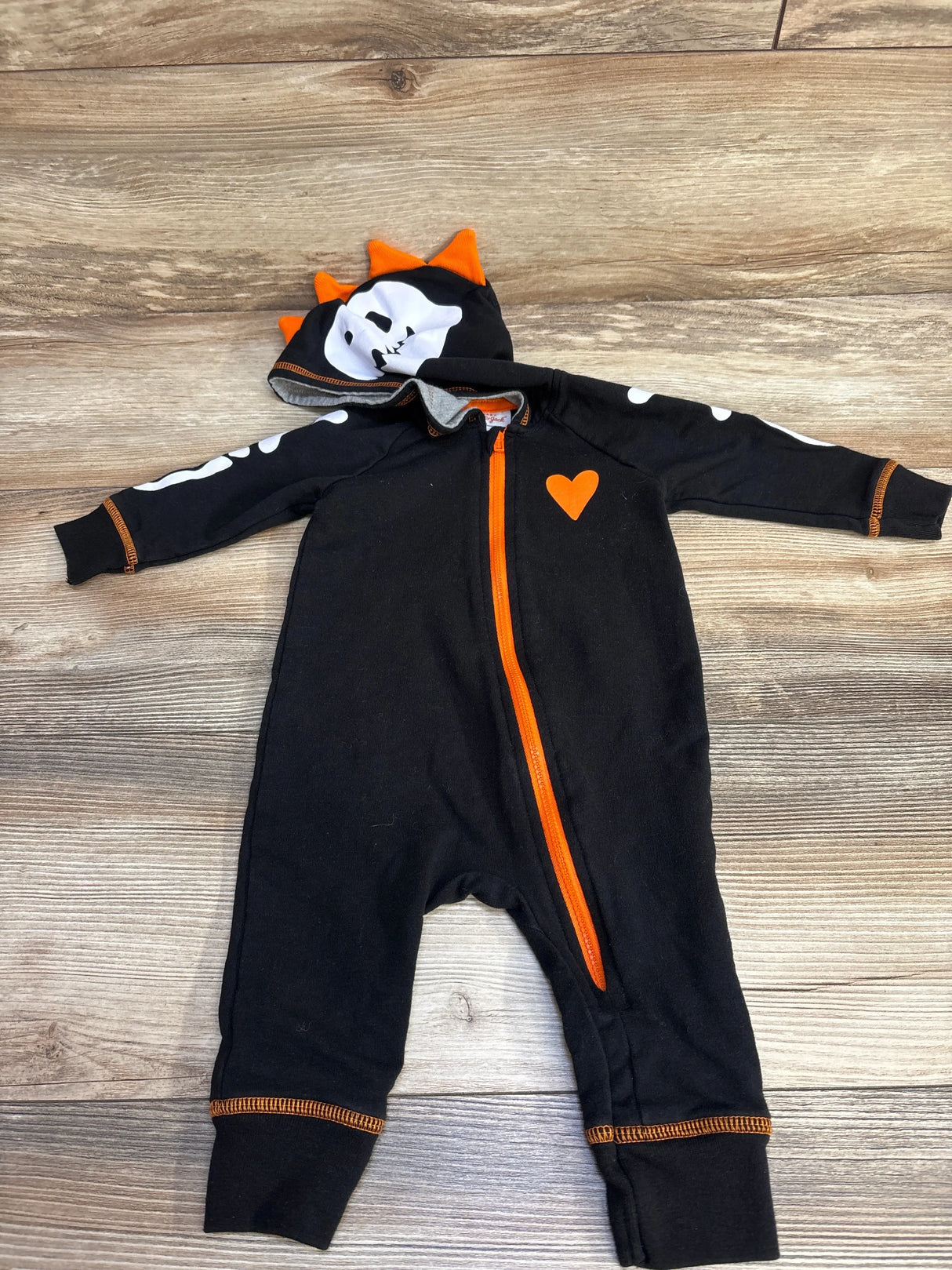 Black Halloween baby onesie with orange zipper, skull hood, and heart detail on wood floor