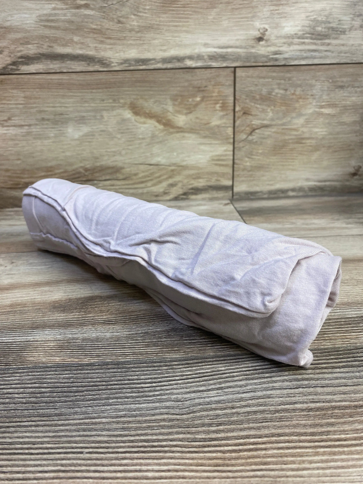 Angled view of Little Unicorn stretch knit viscose swaddle blanket showcasing its rolled shape on a wood-look floor