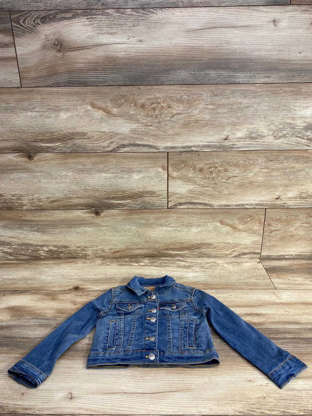 Children's blue denim jacket with button front and pockets on wood background