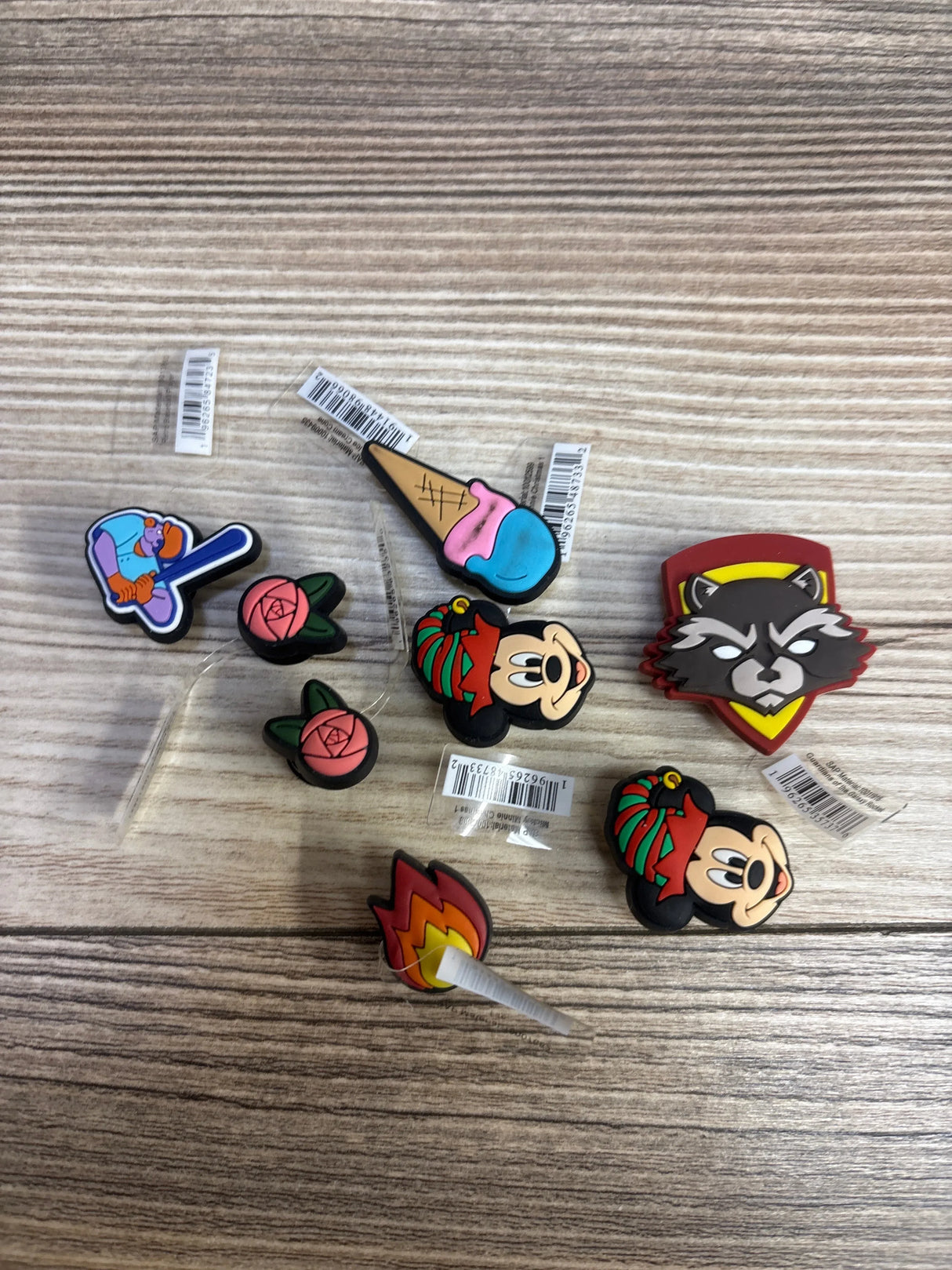 collection of colorful cartoon character pins including Mickey Mouse, raccoon, ice cream cone, baseball player, rose, and flame on wooden surface