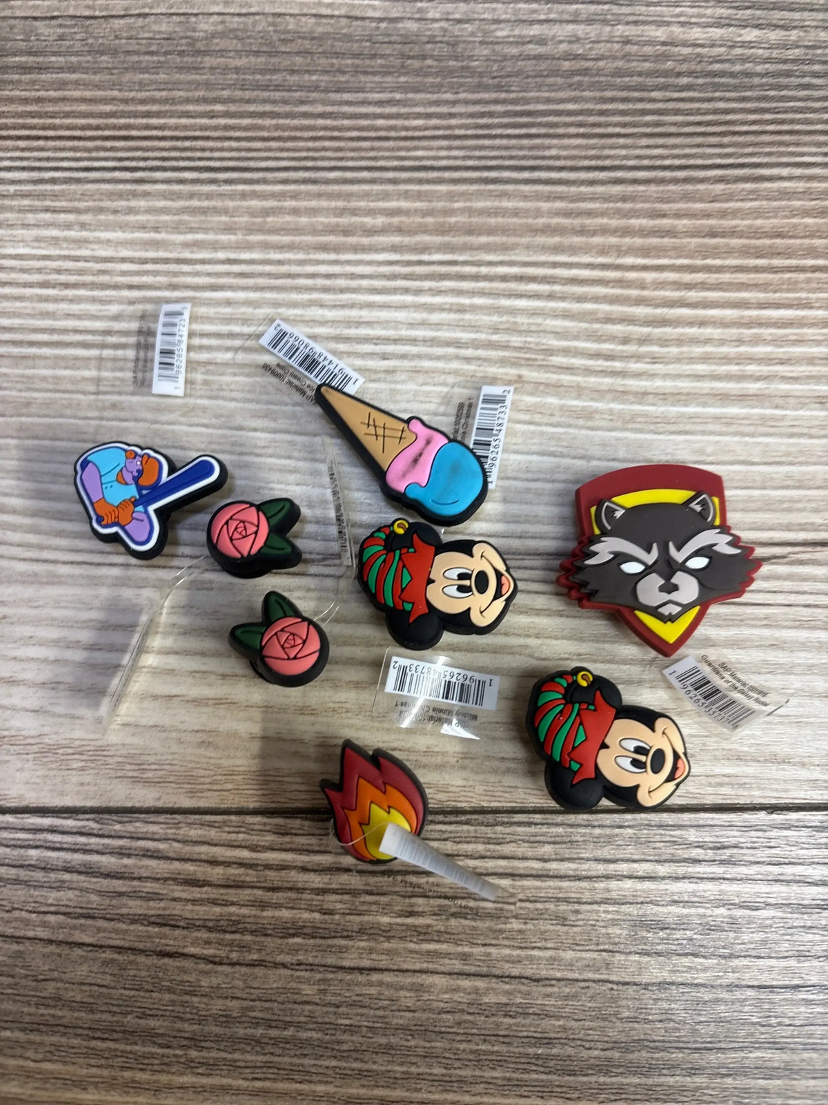 Top view of Crocs Jibbitz 15pk showcasing Mickey Mouse, Guardians of the Galaxy, and retro baseball player charms on wood