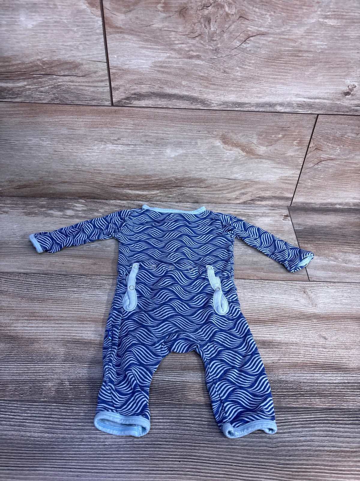 Front view of Kickee Pants Kite Water Lattice bamboo snap coverall in blue, showing long sleeves and snap closures against wood