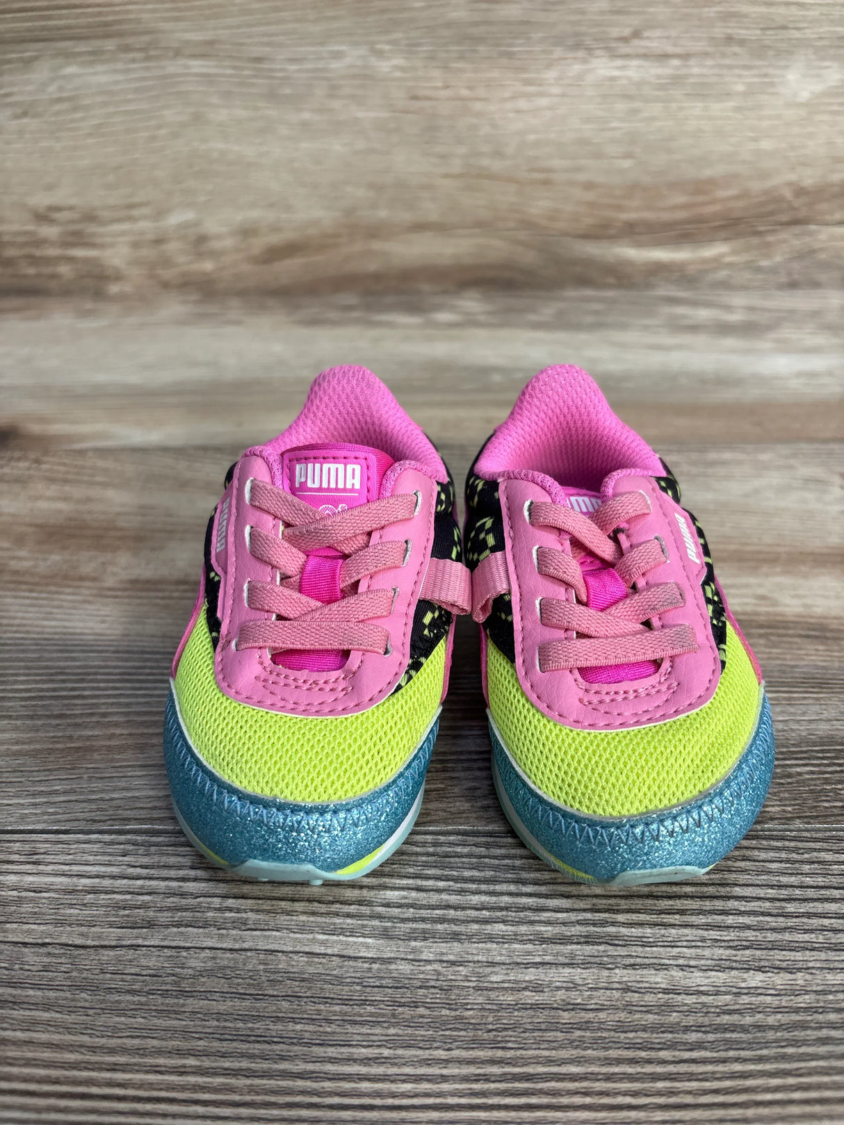 Pair of colorful Puma toddler sneakers with pink, yellow, black, and blue details on wood floor