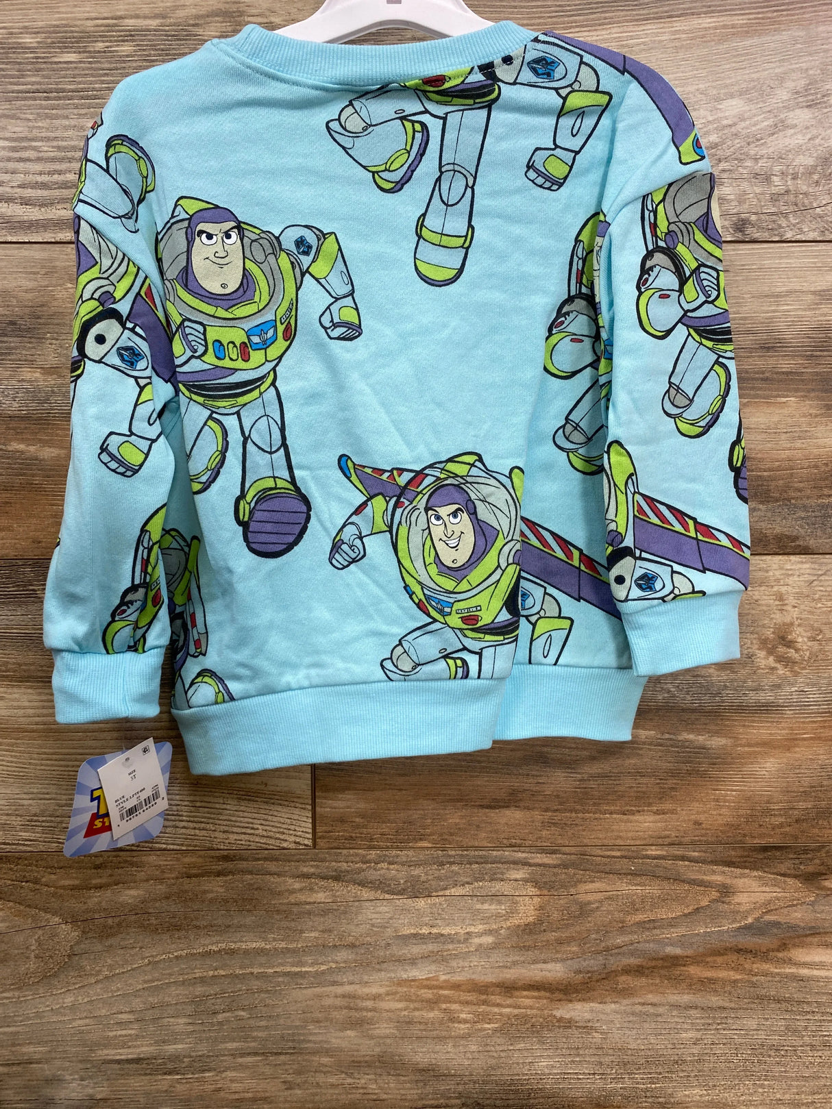Light blue kids sweatshirt with multiple Buzz Lightyear prints from Toy Story, displayed on wooden floor