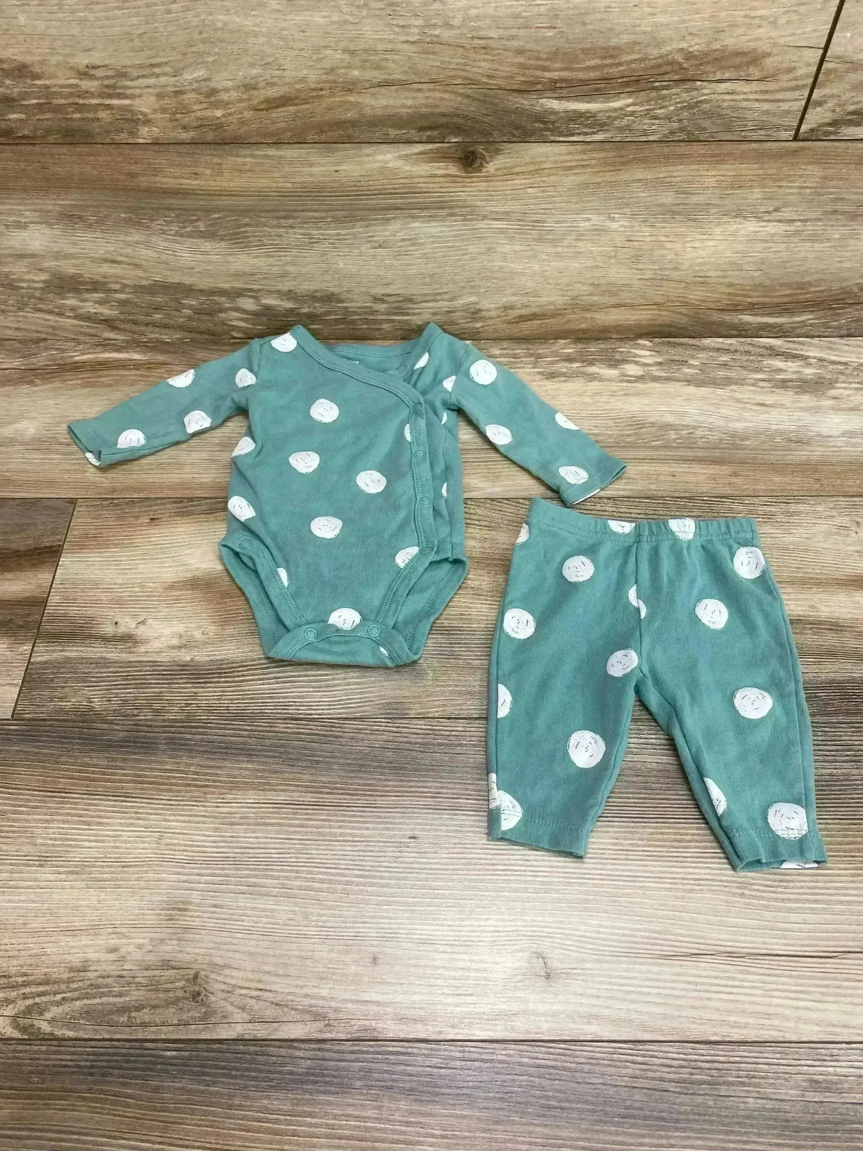 Top-down view of green baby kimono bodysuit and pants with white round dots, snap front and elastic waist on wood background