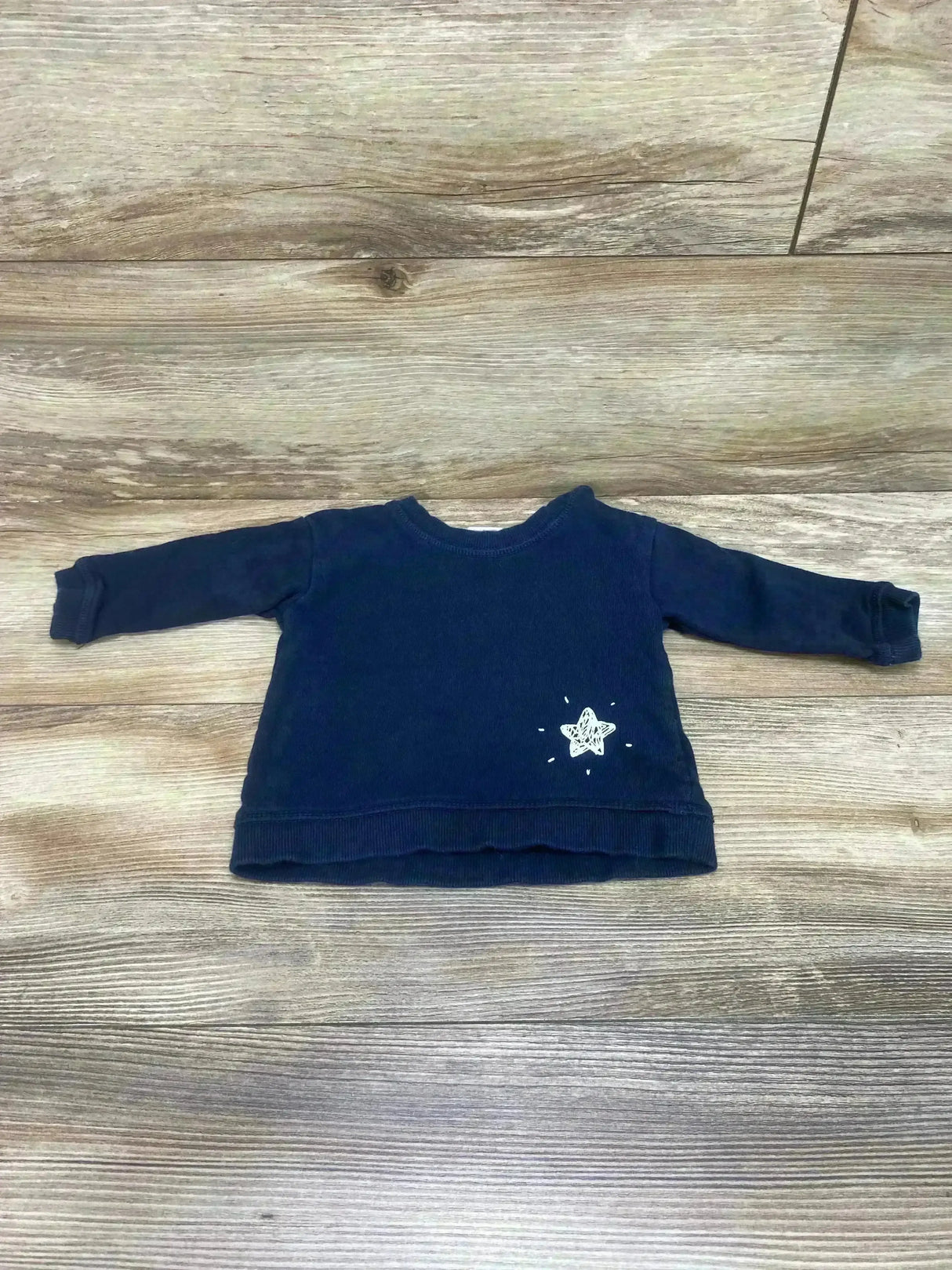 Flat lay of H&M Star Sweatshirt sz 4-6m in navy with small white star graphic and ribbed cuffs on wood plank floor