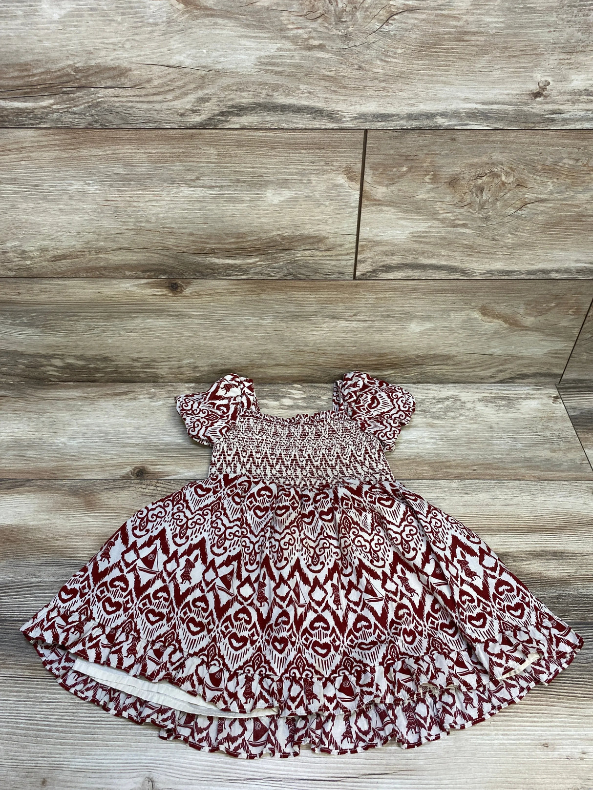 Cute toddler dress with red and white tribal pattern and puff sleeves on wooden floor