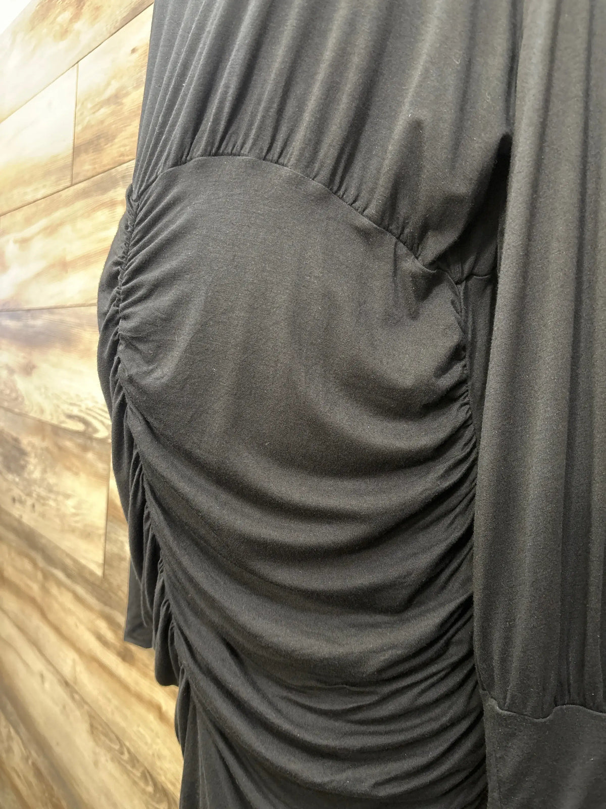 Close-up of black ruched maternity dress with side gathering against wood background
