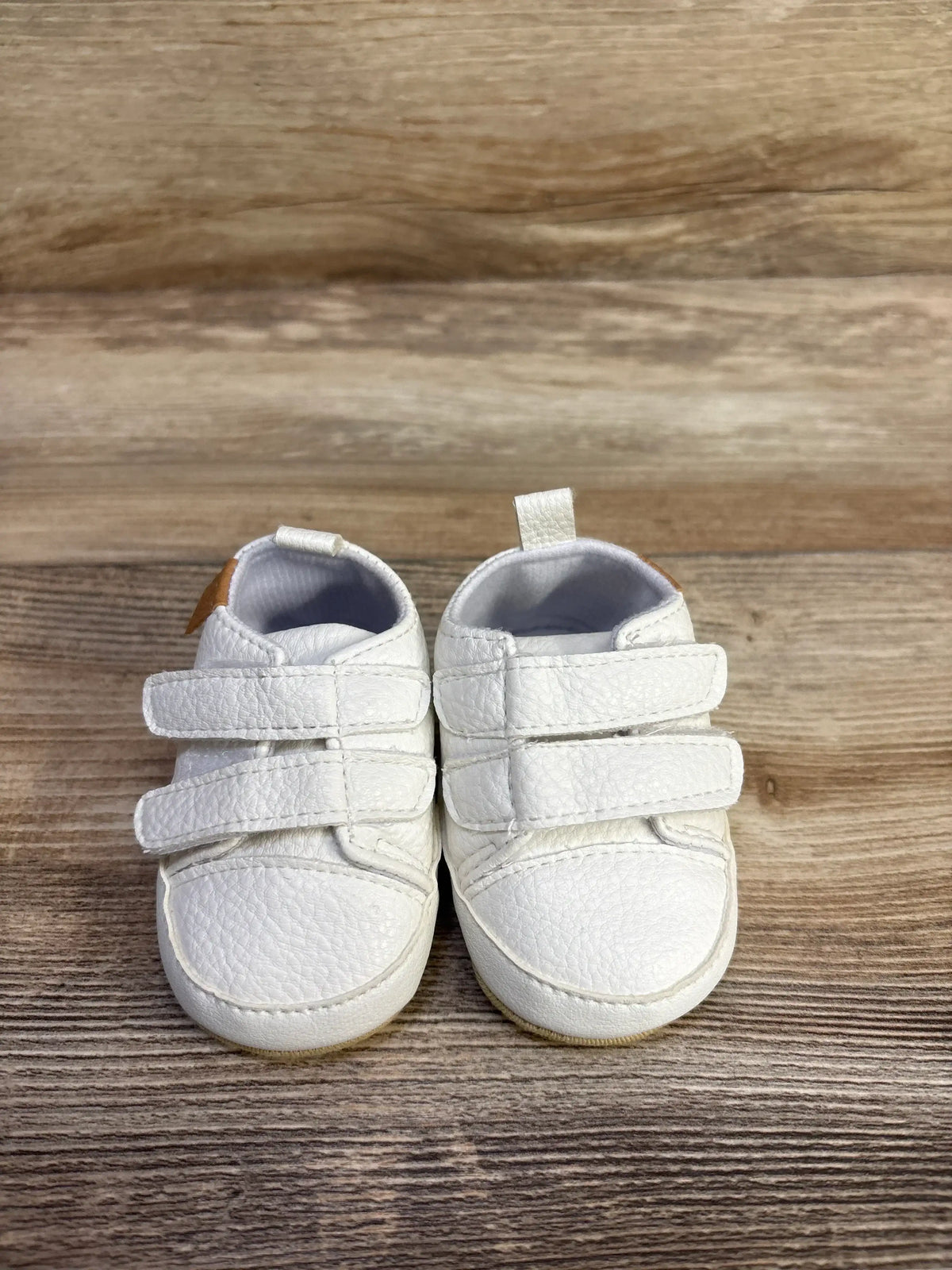 Front view of Myggpp First Walker baby sneakers showing dual velcro straps and pebbled white upper on wood background