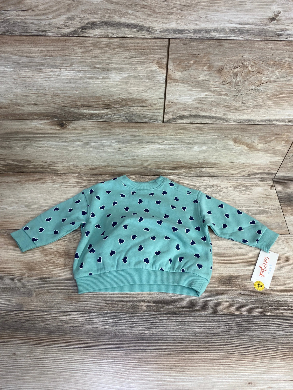 Light blue baby sweater with navy heart pattern, long sleeves, and ribbed cuffs on wooden floor background