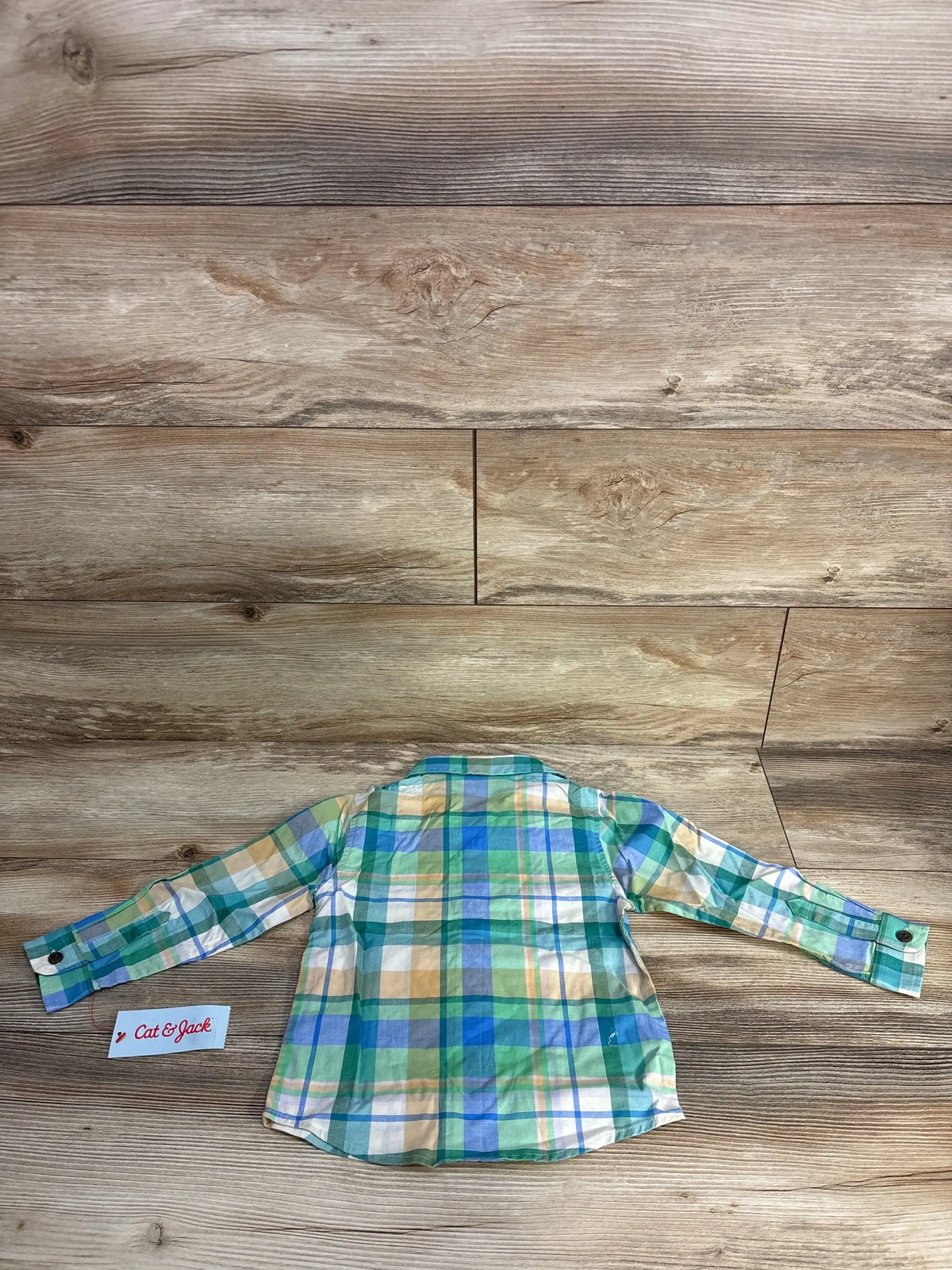 Back view of green, blue, yellow plaid long sleeve button-up shirt for kids on wooden floor