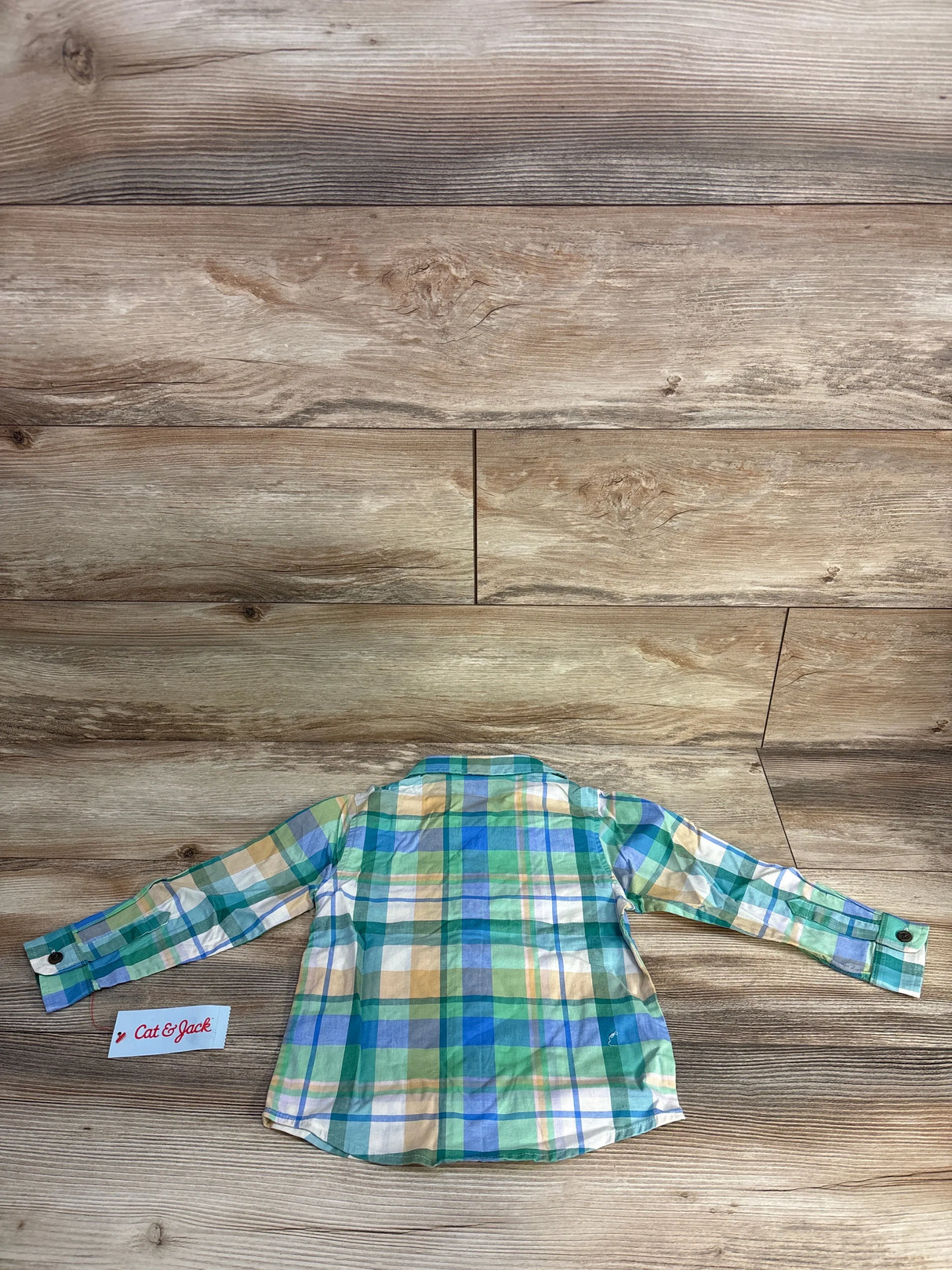 Back view of green, blue, yellow plaid long sleeve button-up shirt for kids on wooden floor