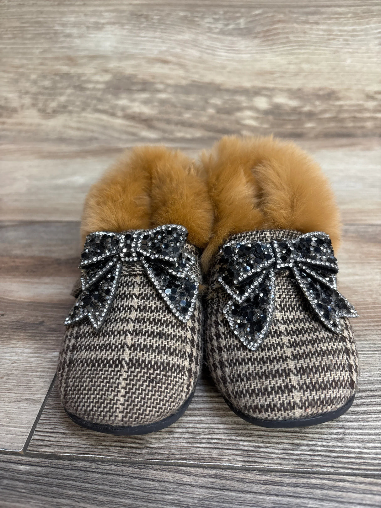 Front view of toddler brown plaid faux-fur lined slippers size 7C showcasing rhinestone bow embellishments on wood floor