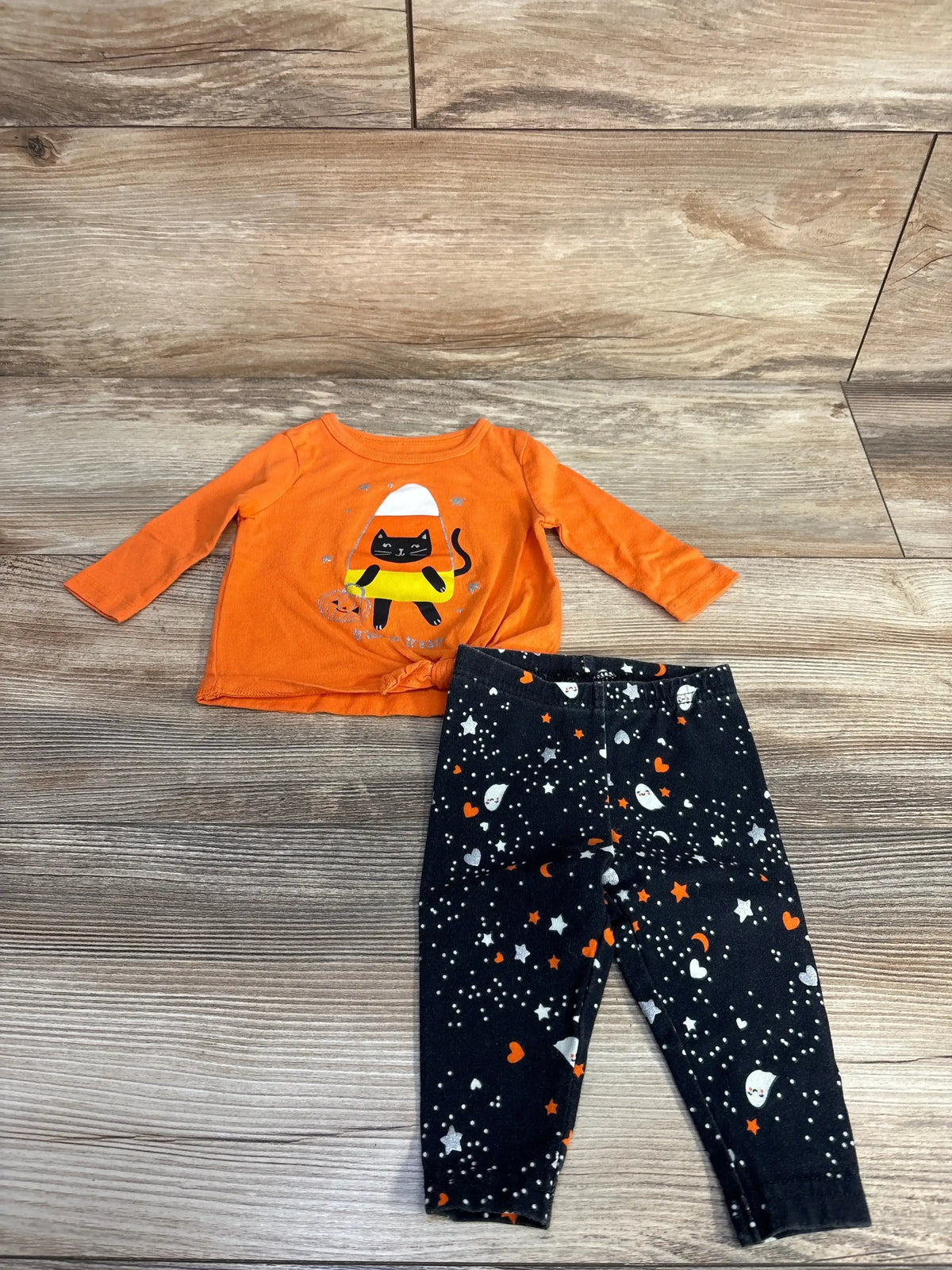Top down view of Carters 2pc Candy Corn shirt and leggings showcasing an orange cat shirt and Halloween print leggings on wood flooring