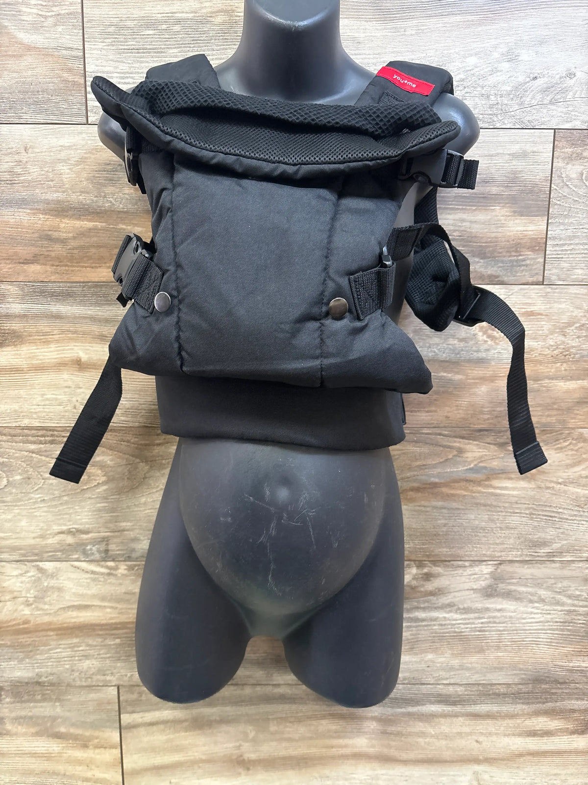 Front view of YOU+ME 4-in-1 Lightweight Mesh Baby Carrier showcasing black mesh fabric and adjustable straps with a wood plank background