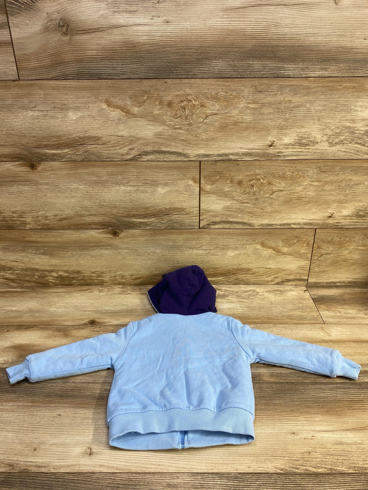 Back view of a light blue full zip jacket with a purple lined hood for toddlers.