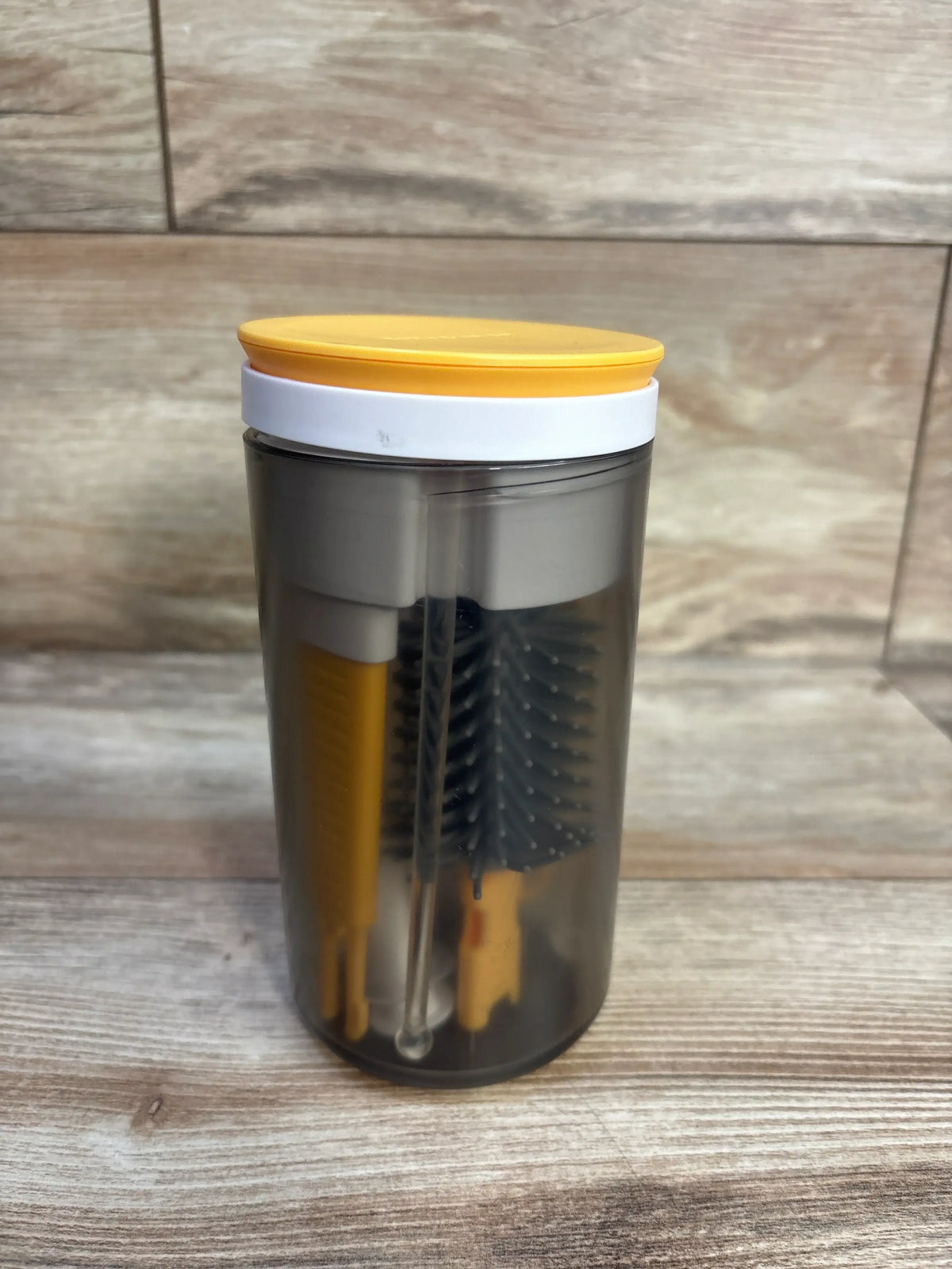 Front view of JoviKids 6-in-1 Portable Bottle Brush Set in a transparent case with yellow lid on wood-look tile