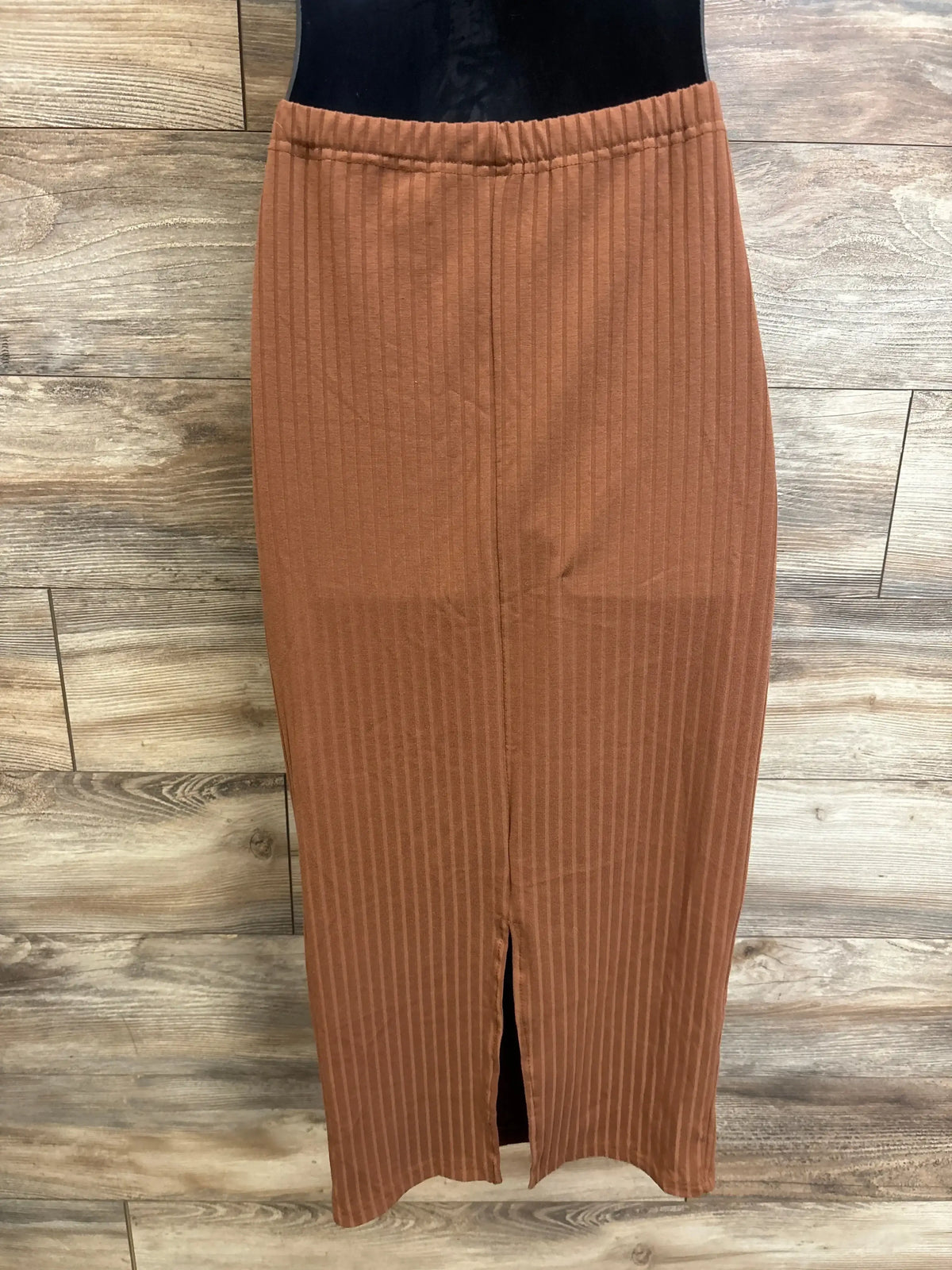 Front view of brown ribbed maternity skirt with elastic waistband and center slit against wood plank background