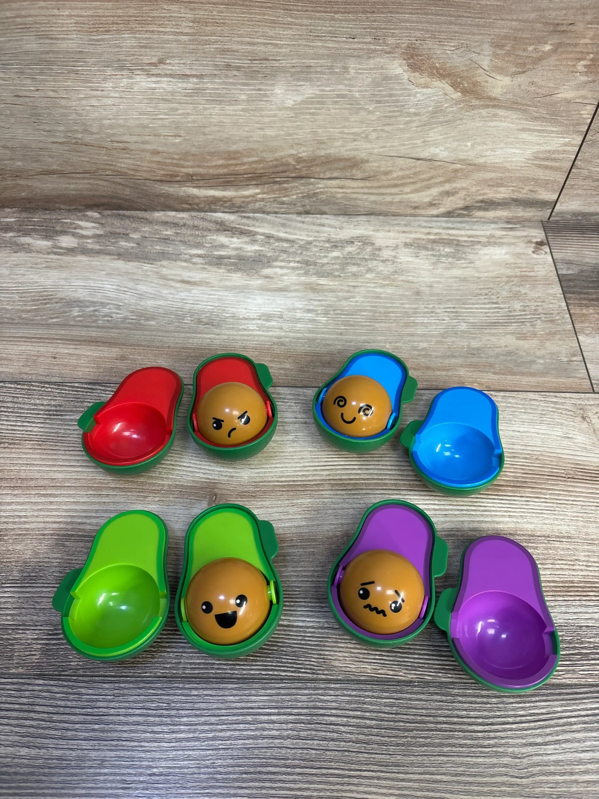 Colorful avocado toy halves with expressive faces on wooden background