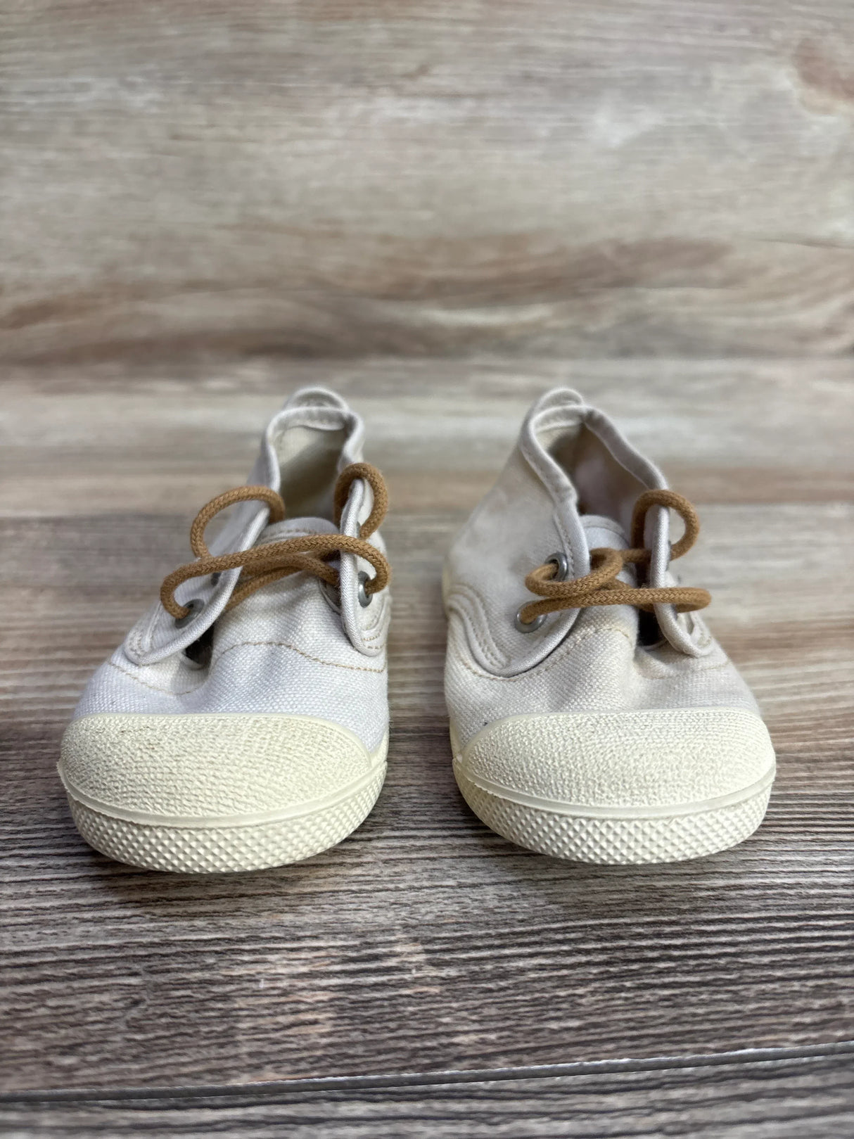 Pair of beige baby canvas shoes with brown laces on wooden surface