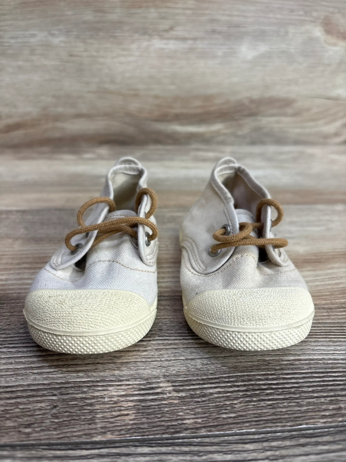Pair of beige baby canvas shoes with brown laces on wooden surface