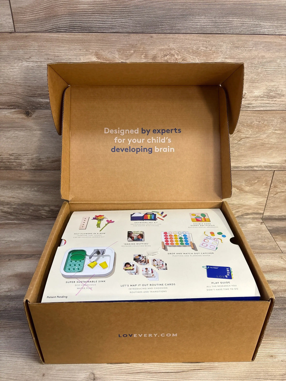 Open view of The Helper Play Kit showing interior flap text Designed by experts for your child's developing brain on wood