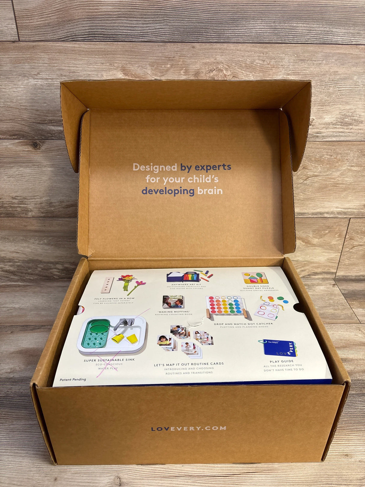 Open view of The Helper Play Kit showing interior flap text Designed by experts for your child's developing brain on wood
