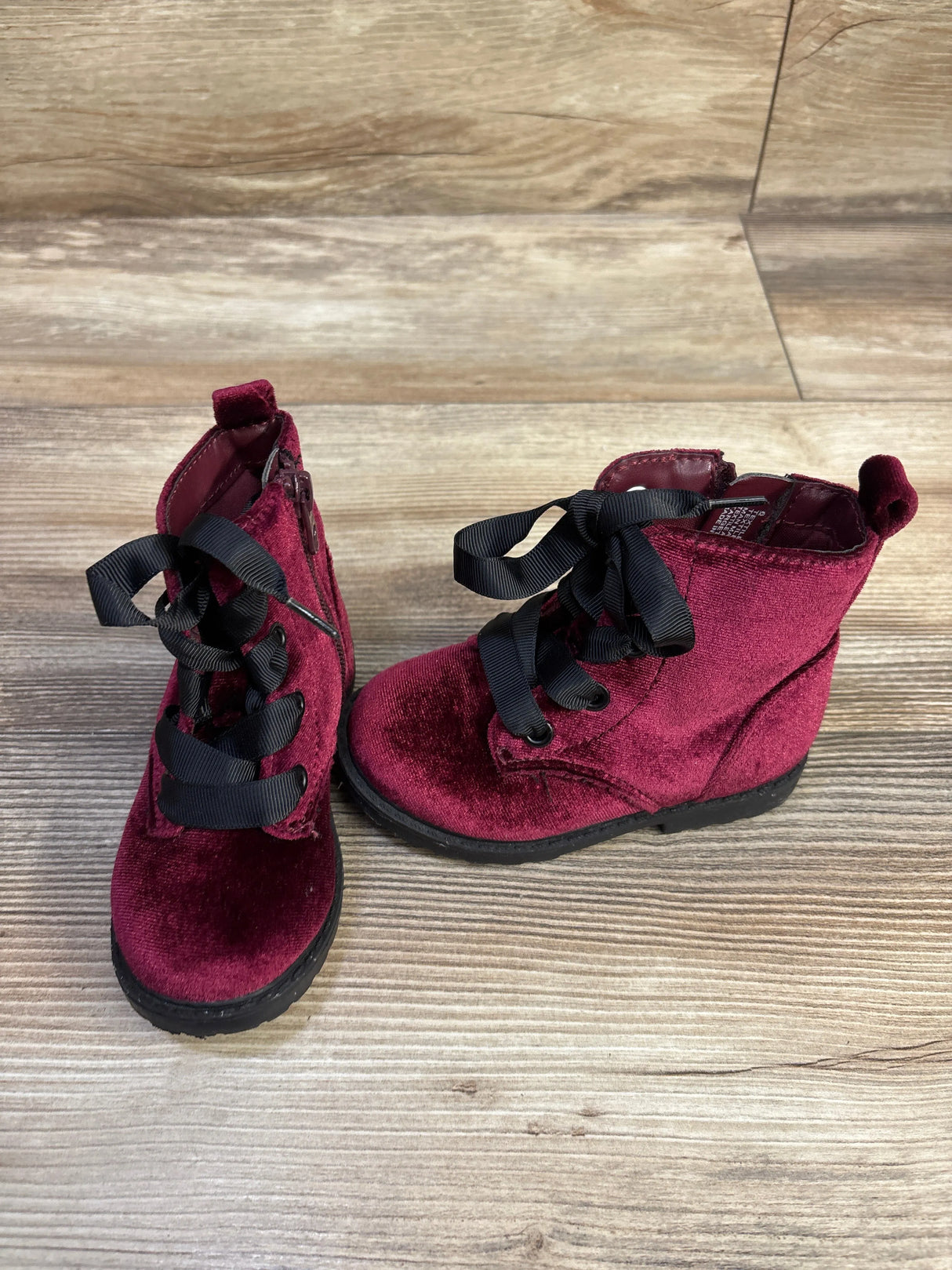Three-quarter view of Cat & Jack toddler velvet boots in burgundy with black ribbon laces on light wood background