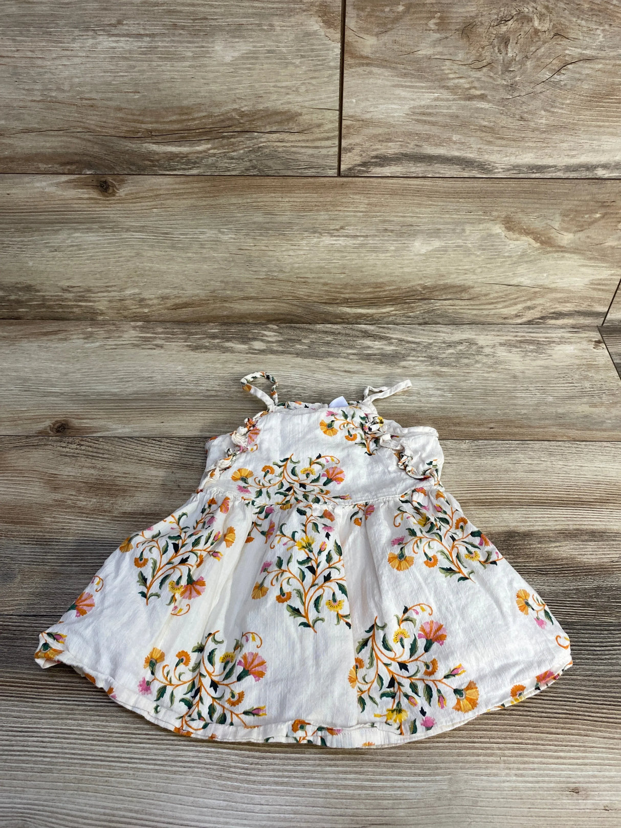 Flat lay of cream Old Navy toddler dress showcasing floral embroidery, ruffle trim, and shoulder ties on wood background