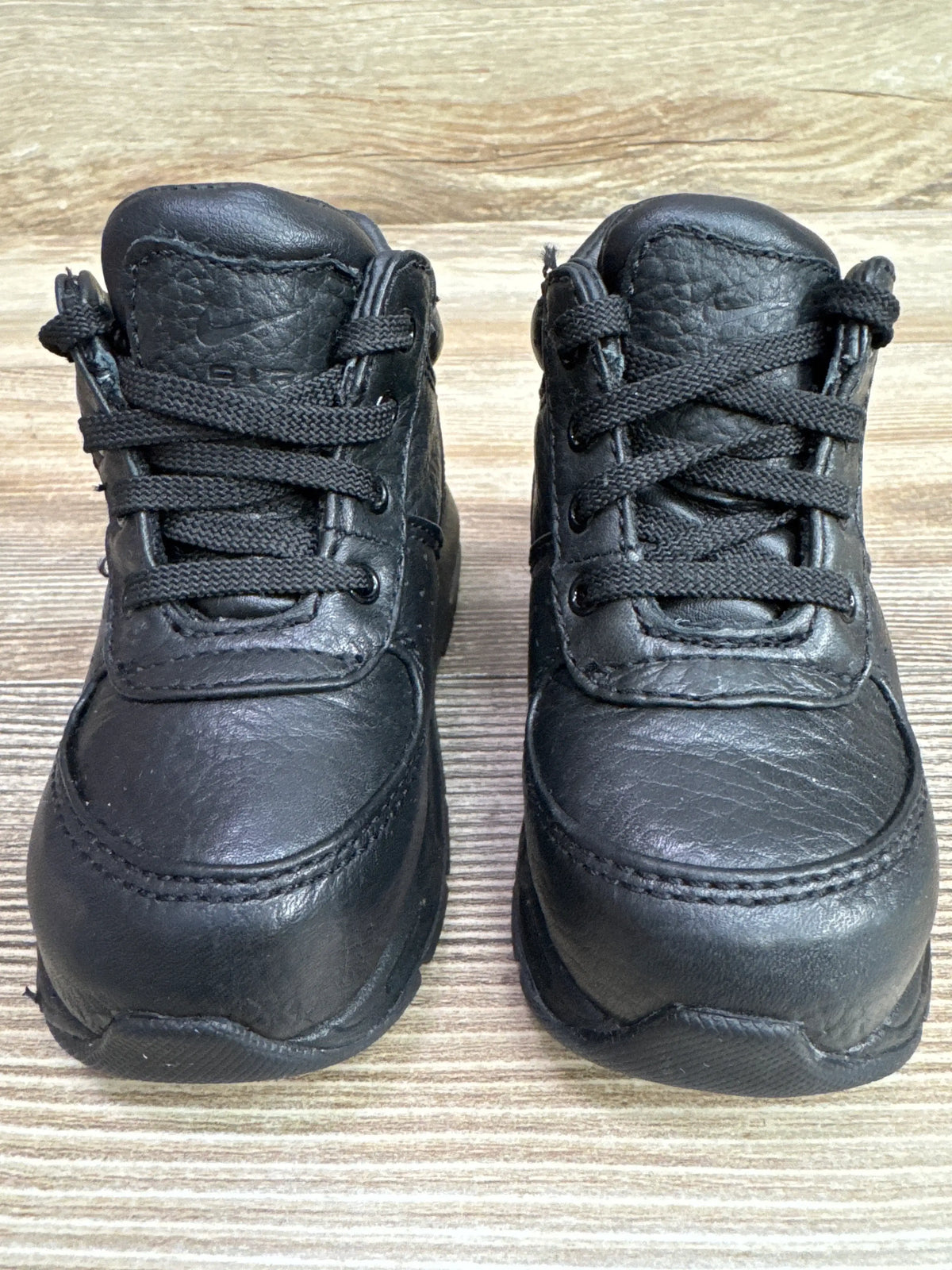 Front view of Nike Air Max Goadome boots in black showcasing the lace-up high-top design on a wood-grain surface