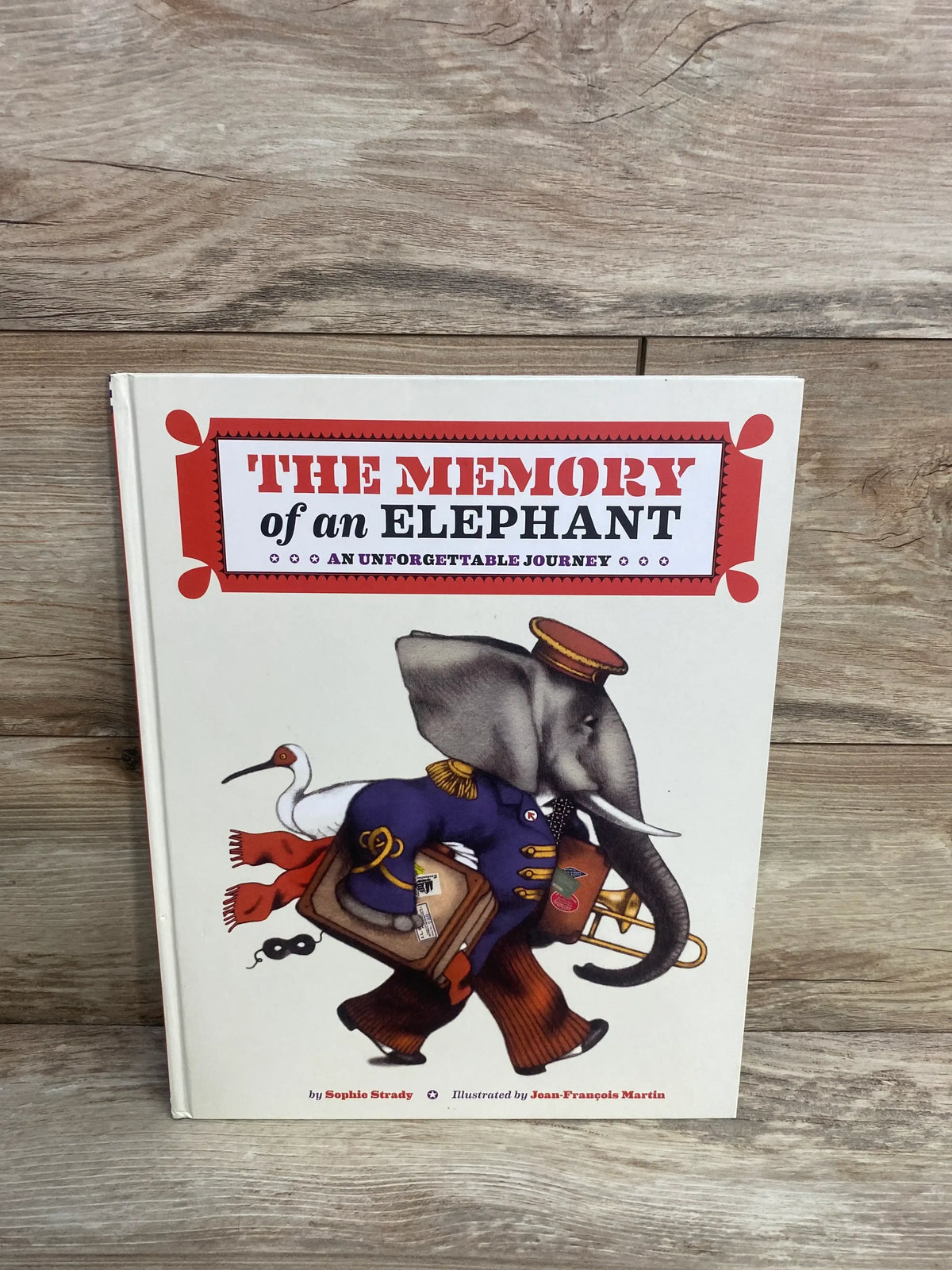 Cover of children’s book The Memory of an Elephant with illustration of elephant in uniform carrying suitcase and trombone