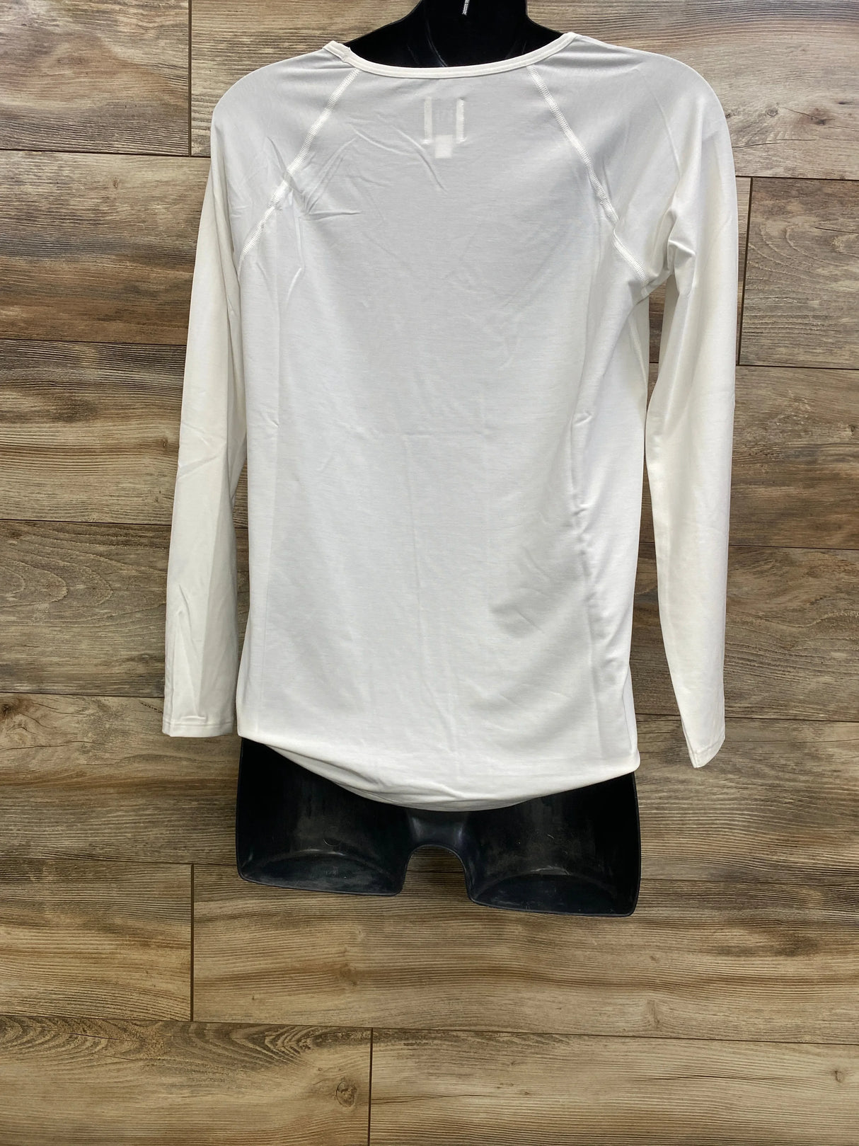 Back view of white Gap Breathe maternity long sleeve shirt (XS) showing raglan seams and curved hem on black mannequin against wood background