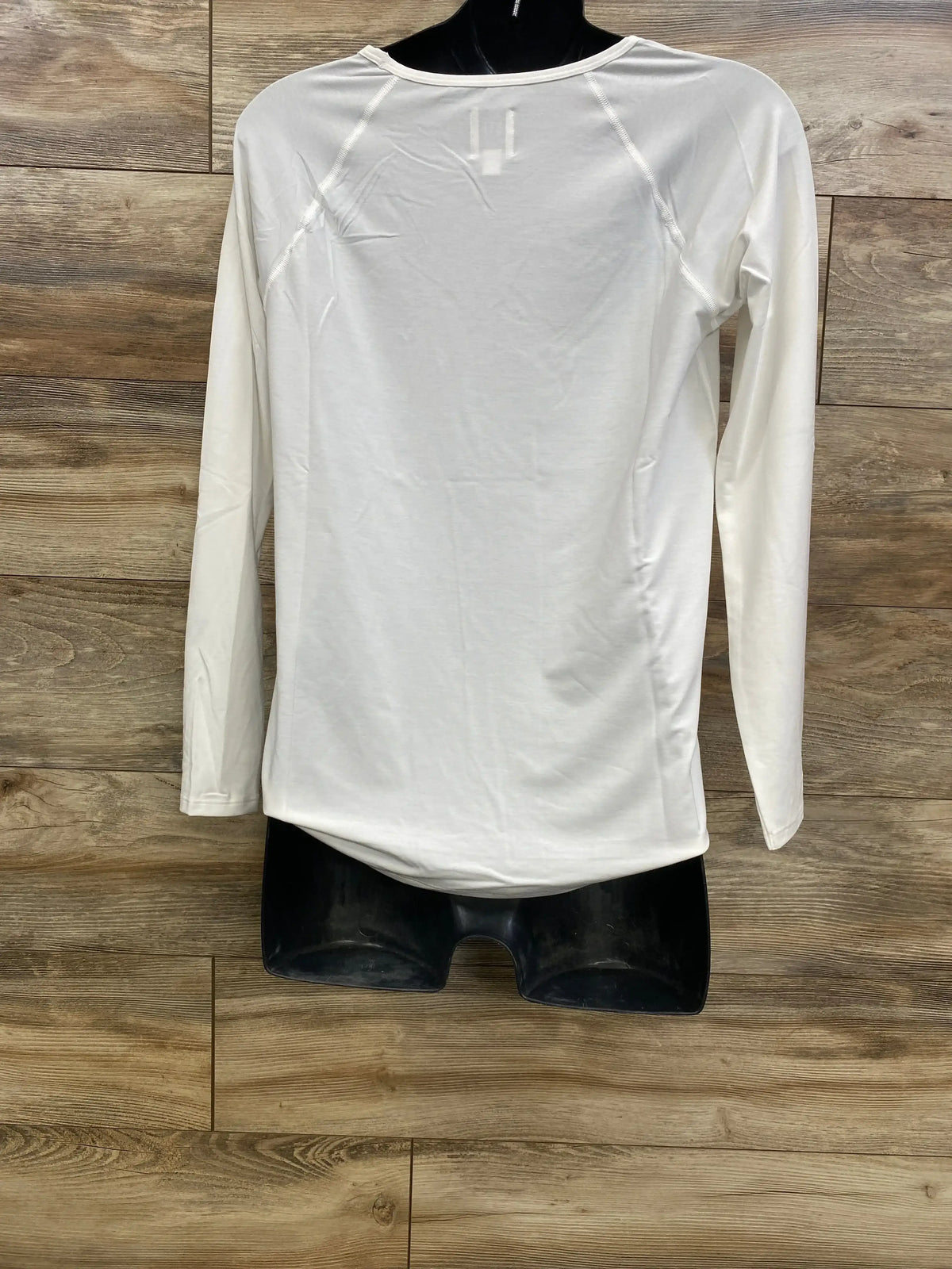 Back view of white Gap Breathe maternity long sleeve shirt (XS) showing raglan seams and curved hem on black mannequin against wood background