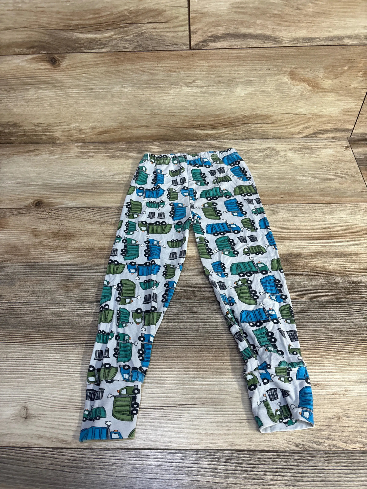 Flat lay of Clover Baby & Kids dump truck viscose pants in blue showcasing elastic waistband and truck print on a wood background