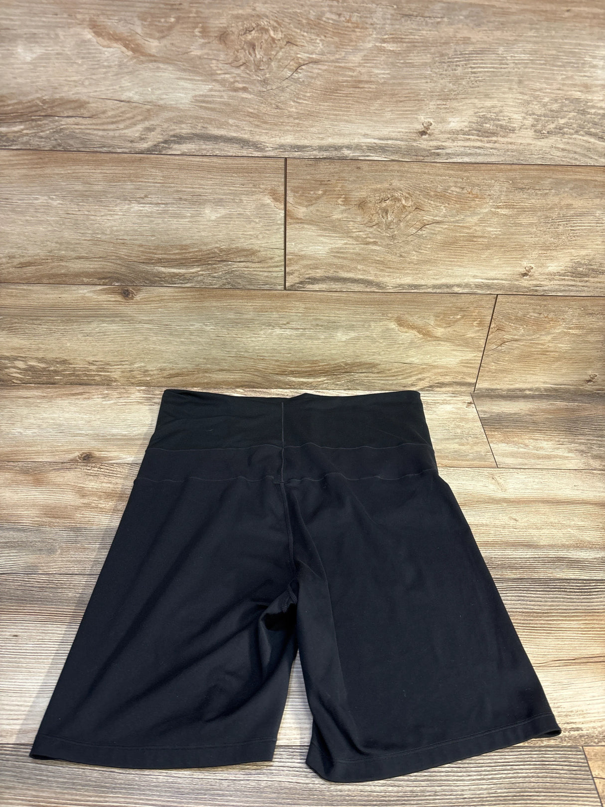 Flat lay of Nike maternity Dri-FIT active shorts showcasing high-rise foldover waistband and knee-length inseam on wood floor background