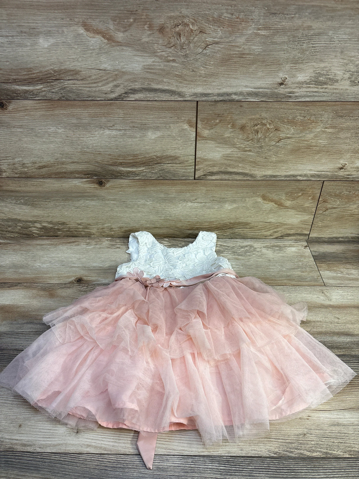 Flat lay of toddler floral dress showcasing white lace bodice, pink layered tulle skirt and tied sash on wood background