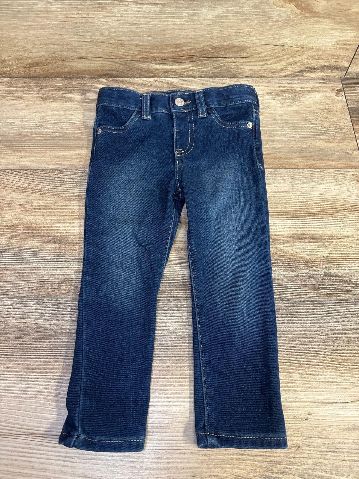 Front view of Cat & Jack toddler blue jeggings size 2T laid flat with straight legs, faded thighs, button waist on wood background